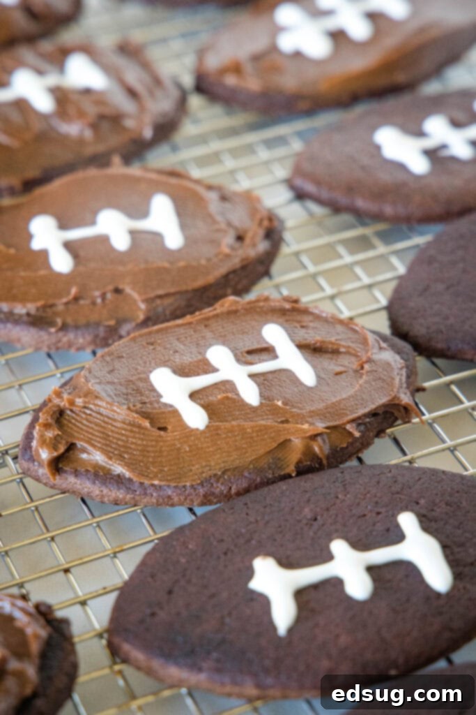Chocolate sugar cookies partially frosted and decorated to look like footballs, arranged on a wire rack.