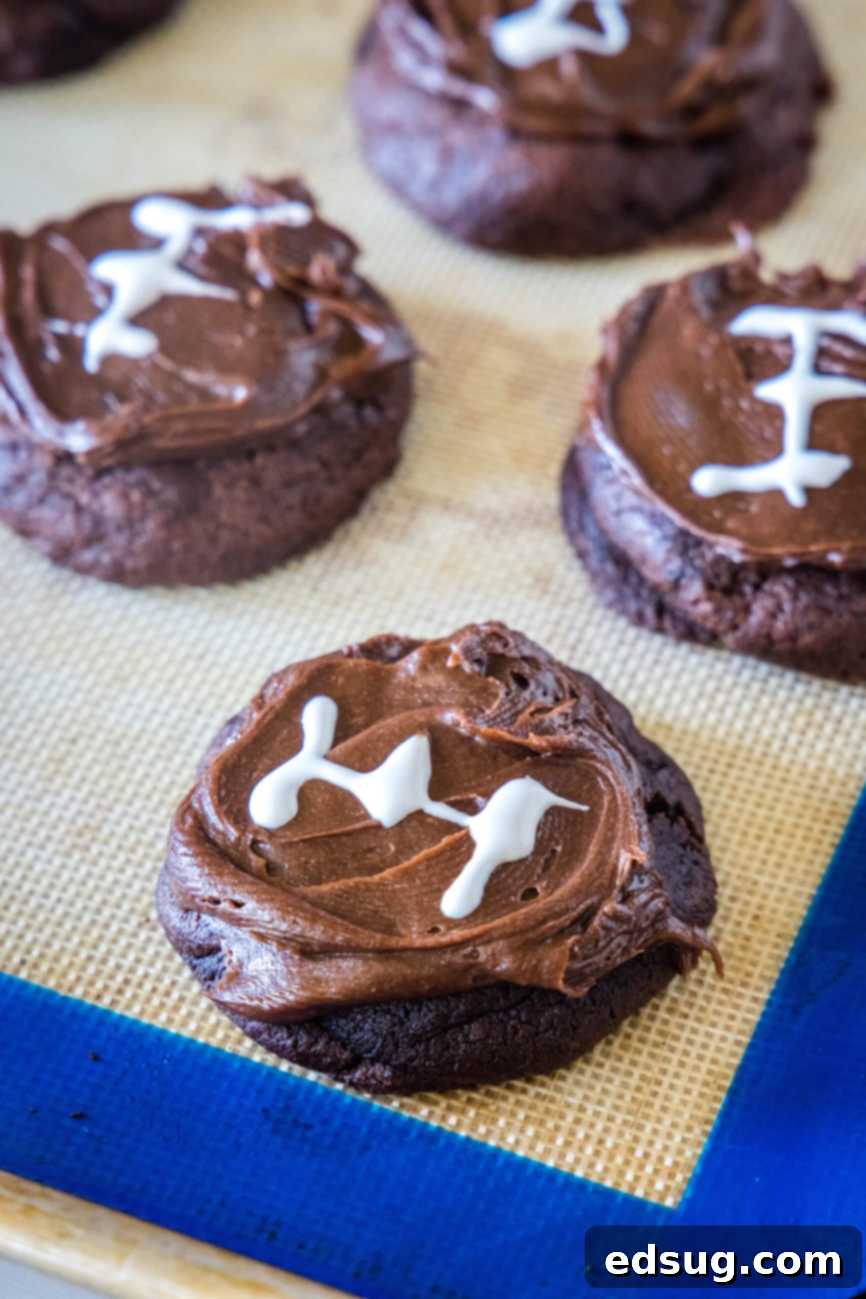 Round chocolate sugar cookies frosted and decorated to look like footballs on a baking mat, showing an alternative shape.