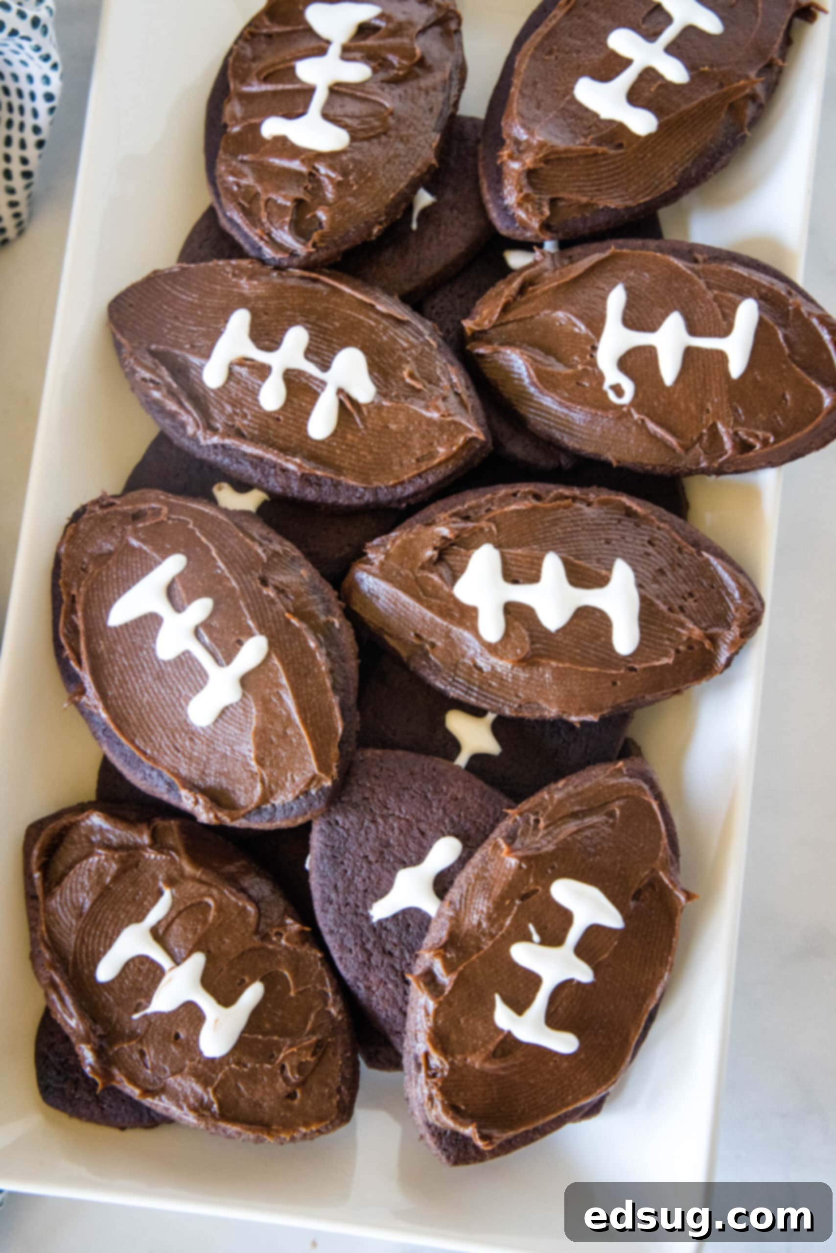 Overhead view of an assortment of frosted football cookies neatly arranged on a rectangular white plate.