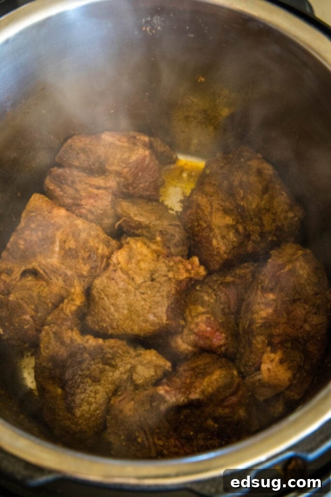 Smoky, juicy Mexican shredded beef is easy to make in the Instant Pot or Crock Pot! Perfect in tacos, enchiladas, or served over rice. Beef chuck roast pieces browning inside the instant pot.