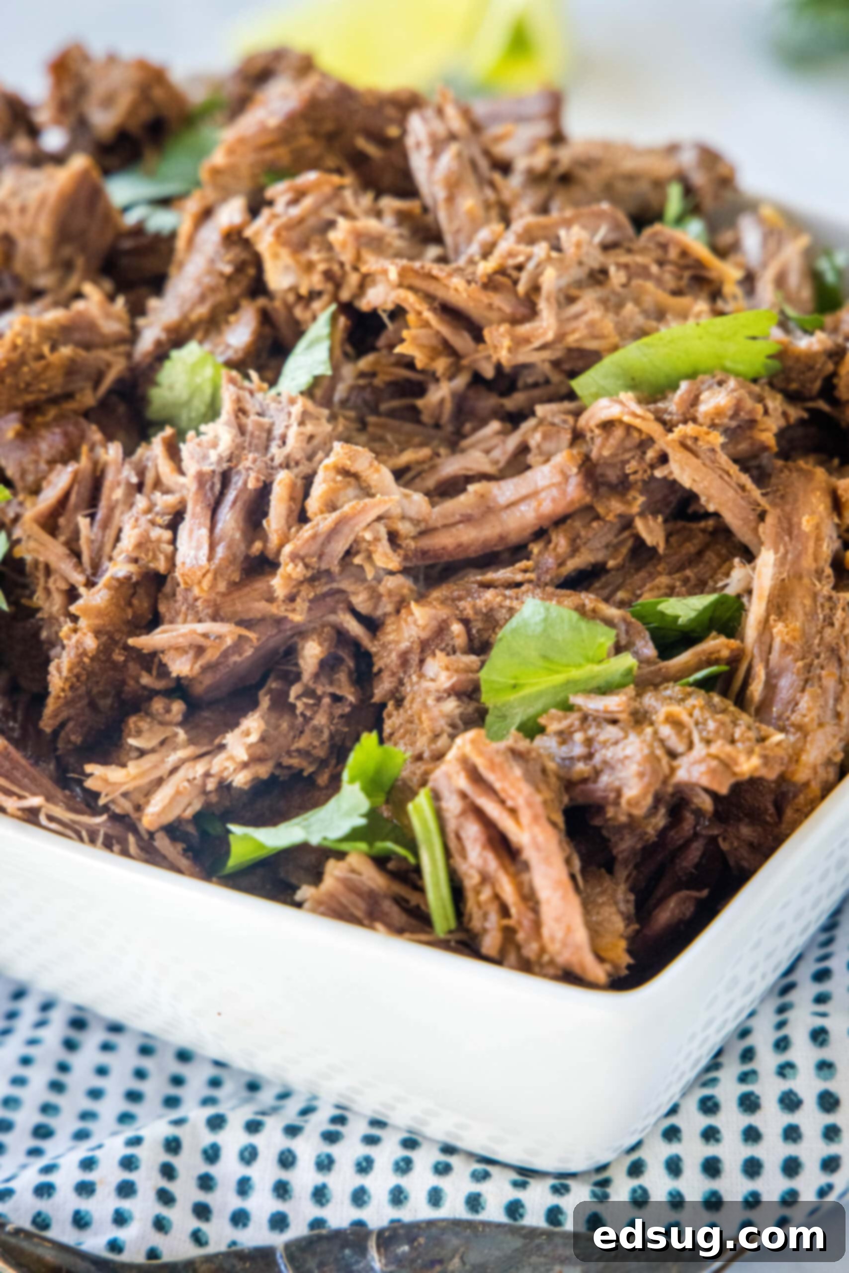Smoky, juicy Mexican shredded beef is easy to make in the Instant Pot or Crock Pot! Perfect in tacos, enchiladas, or served over rice. Mexican shredded beef in a square bowl garnished with cilantro and a lime wedge.