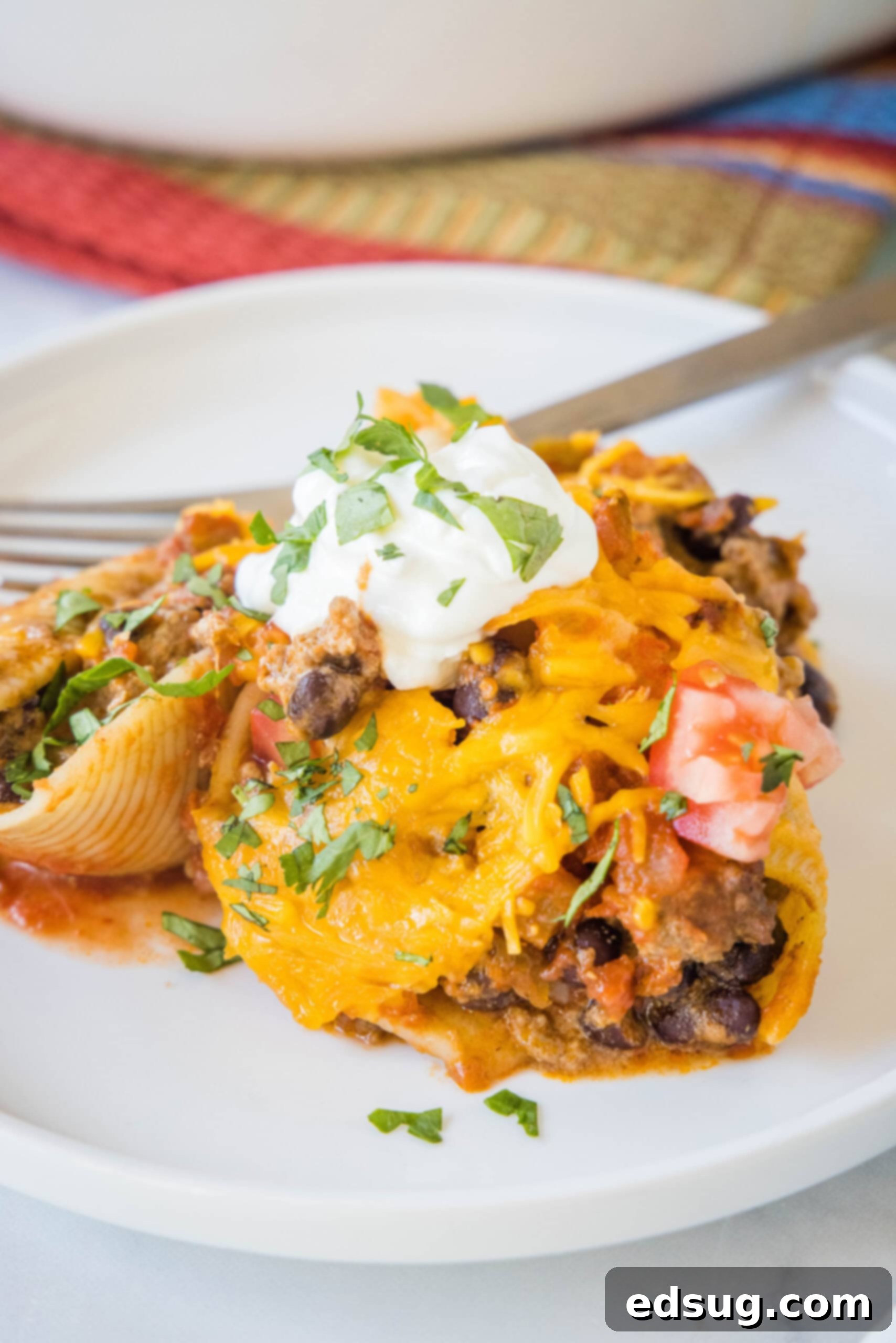 Cheesy taco stuffed shells are an easy Tex-Mex dinner made from jumbo pasta shells filled with creamy taco beef, salsa, and melty cheese. A serving of taco stuffed shells on a white plate next to a fork.