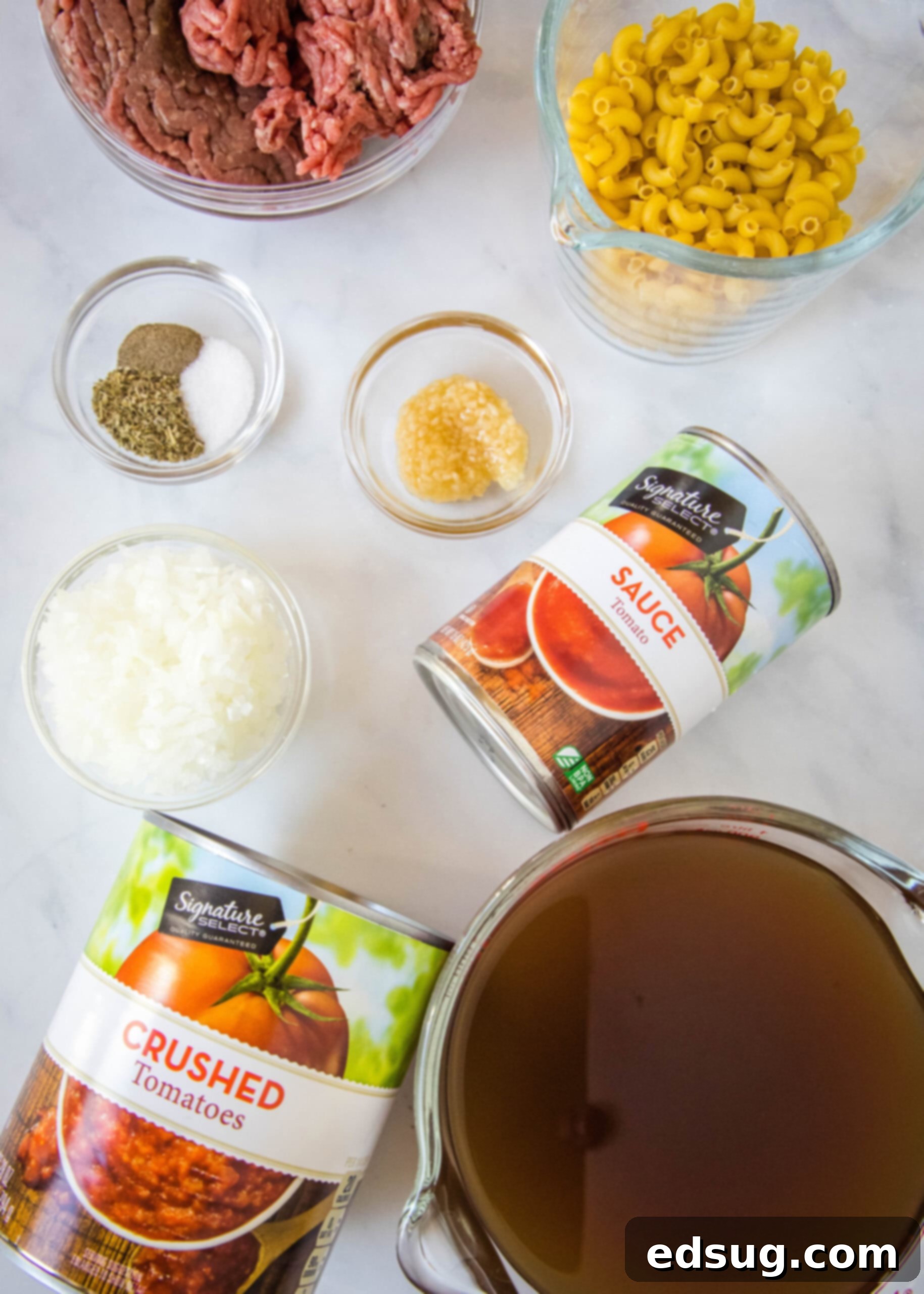 A collection of fresh and canned ingredients, neatly arranged on a wooden surface, ready for making beef and macaroni soup.