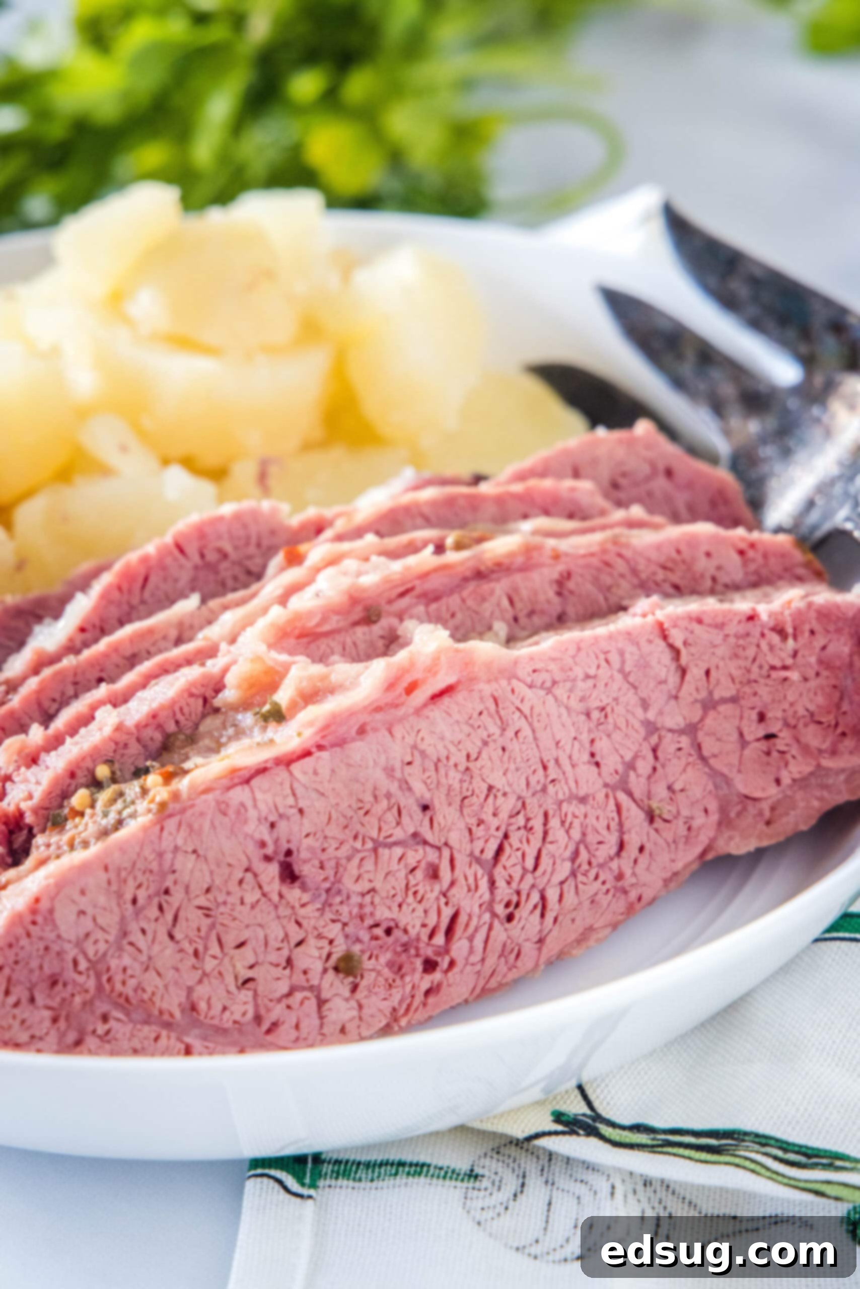 Succulent slices of slow cooker corned beef on a white plate, served with tender cooked onions and a fork.
