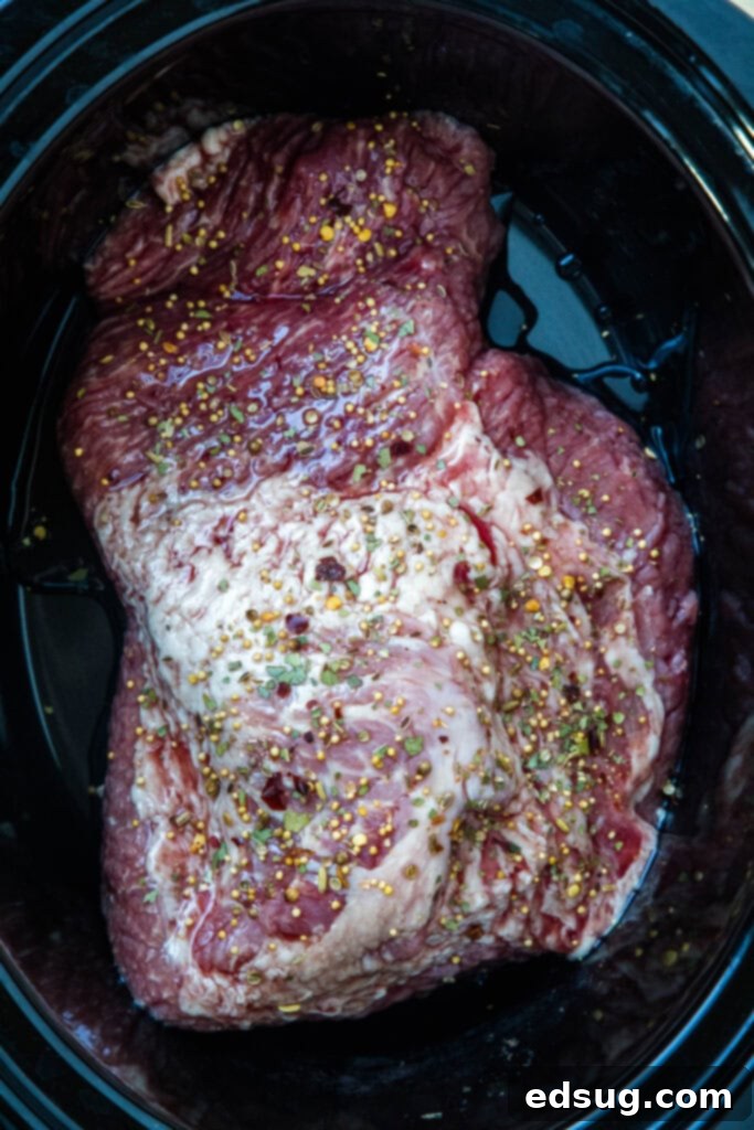 Uncooked corned beef brisket placed inside the slow cooker, ready for seasoning.