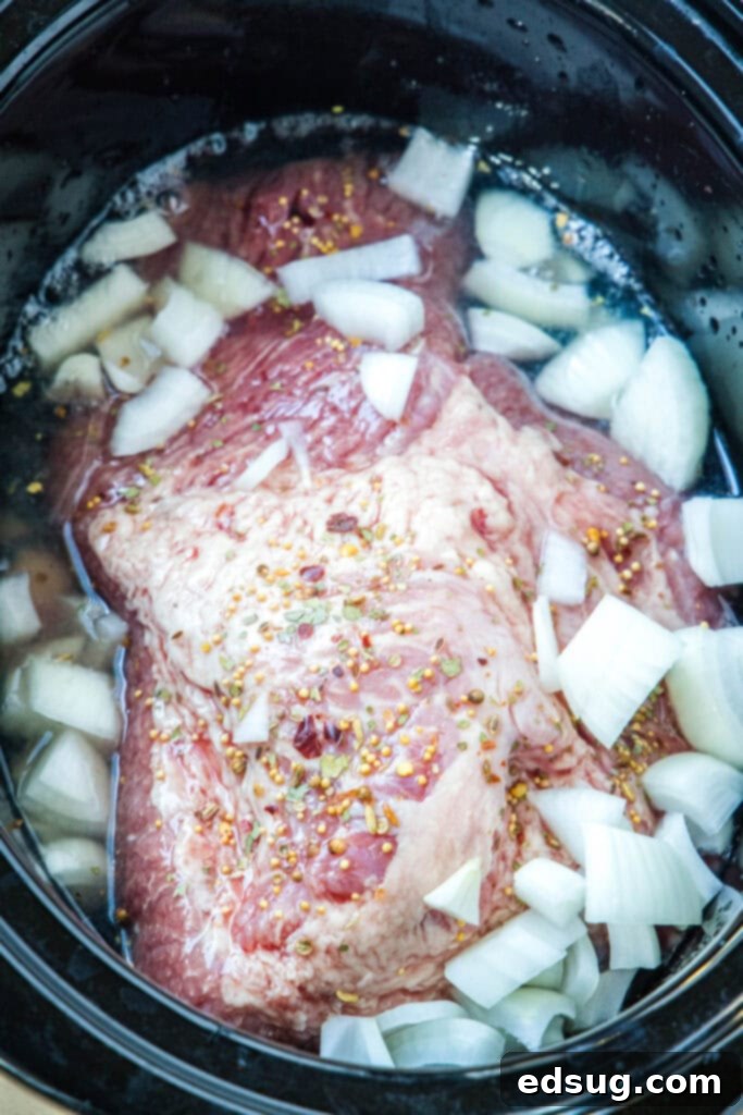 Chopped onions being added over the corned beef brisket and seasoning in the slow cooker.