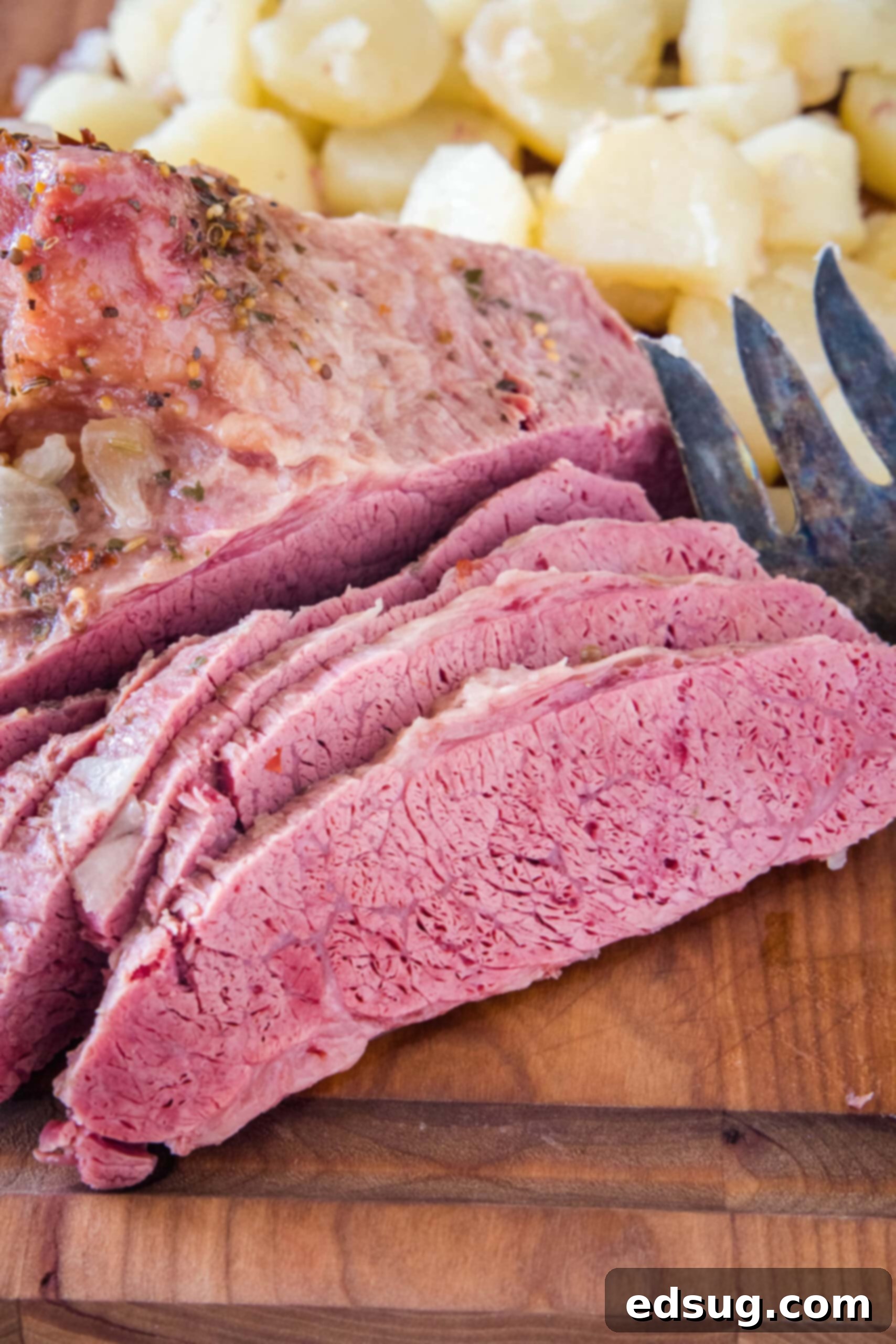 Close-up of perfectly sliced corned beef on a wooden cutting board, with cooked onions on the side.