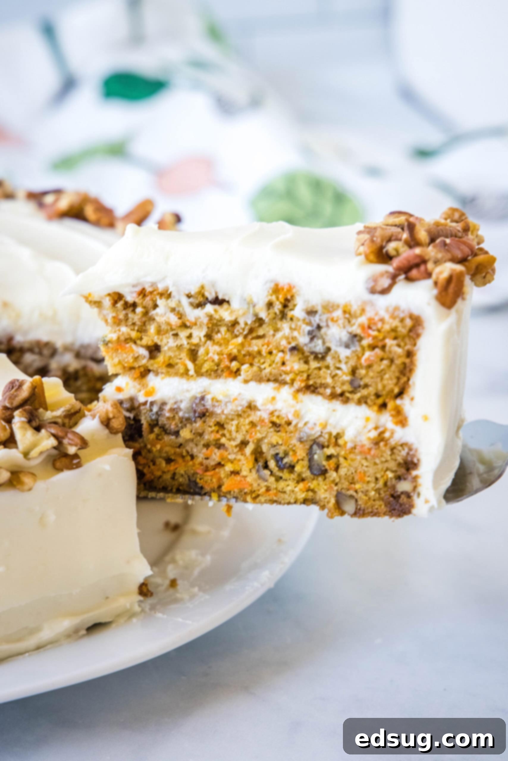 The best homemade carrot cake! Made from moist cake layers loaded with crunchy pecans, filled and frosted with sweet cream cheese frosting. A slice of frosted carrot cake is lifted from the rest of the cake with a cake server.