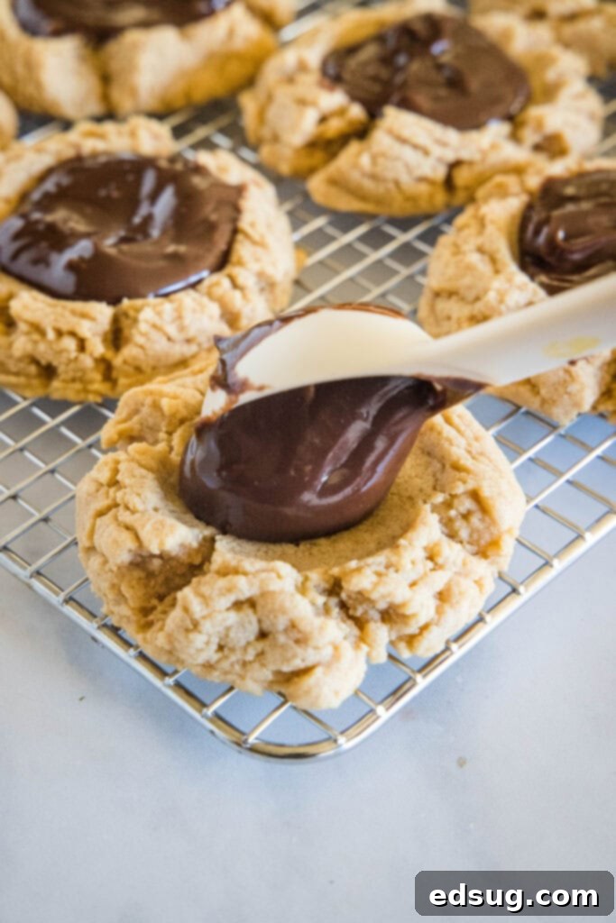 Cocoa Peanut Butter Cloud Cookies 4 Chocolate ganache being carefully spooned into the indentation of a baked peanut butter cookie.