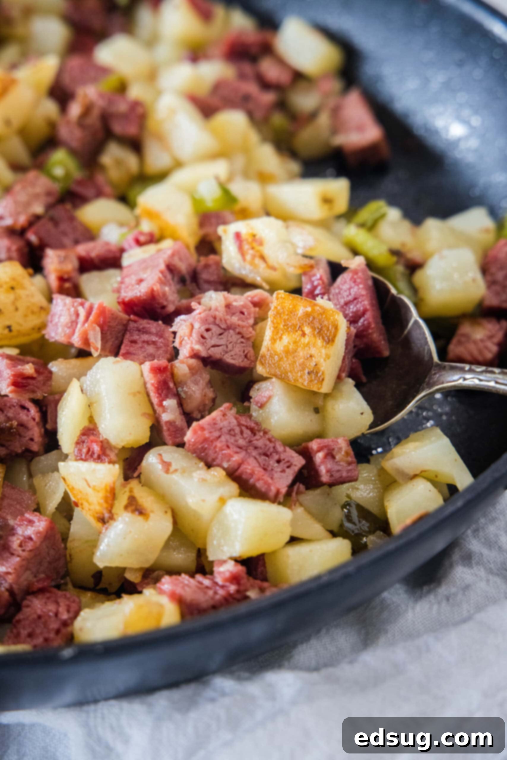 Make homemade corned beef hash with leftover corned beef, tender potatoes, onions, and bell peppers. An easy breakfast, ready in 30 minutes! Close up of golden brown corned beef hash in a skillet with a serving spoon, showcasing crispy textures.