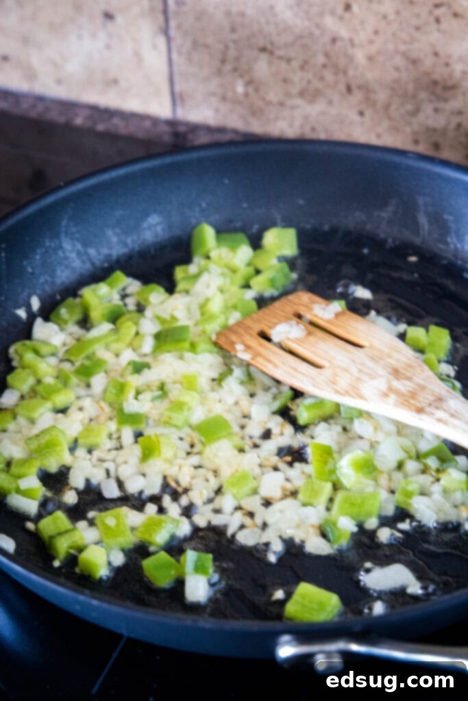 Make homemade corned beef hash with leftover corned beef, tender potatoes, onions, and bell peppers. An easy breakfast, ready in 30 minutes! Diced onions and bell pepper sauteing in a large skillet, with a wooden spatula, turning tender and fragrant.