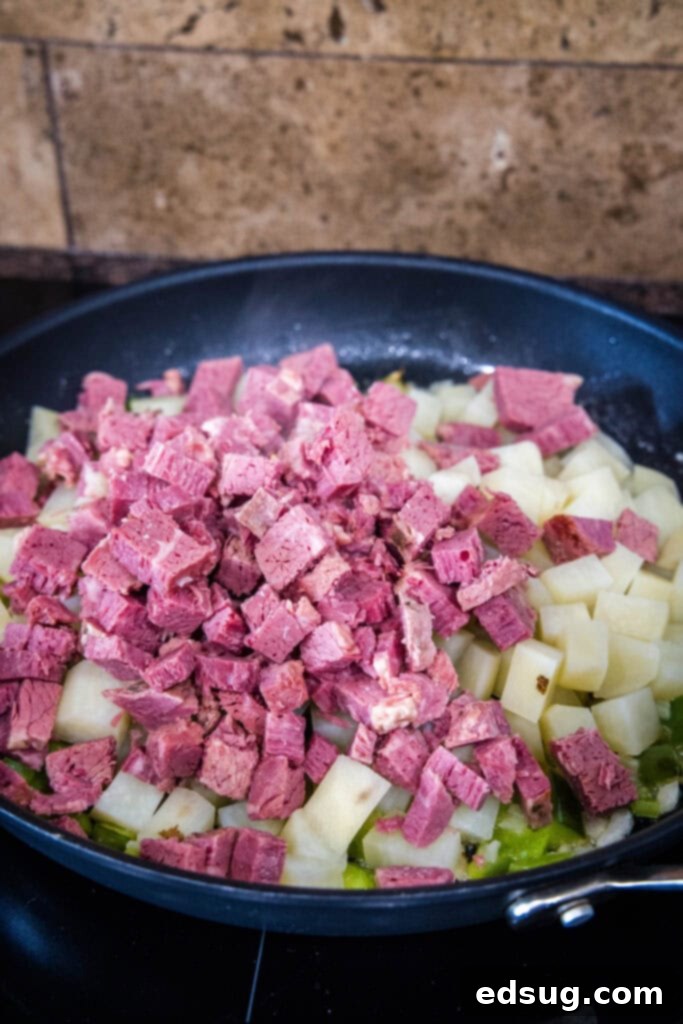 Make homemade corned beef hash with leftover corned beef, tender potatoes, onions, and bell peppers. An easy breakfast, ready in 30 minutes! Chopped corned beef added to a skillet with diced sauteed onions and peppers, ready to be combined.