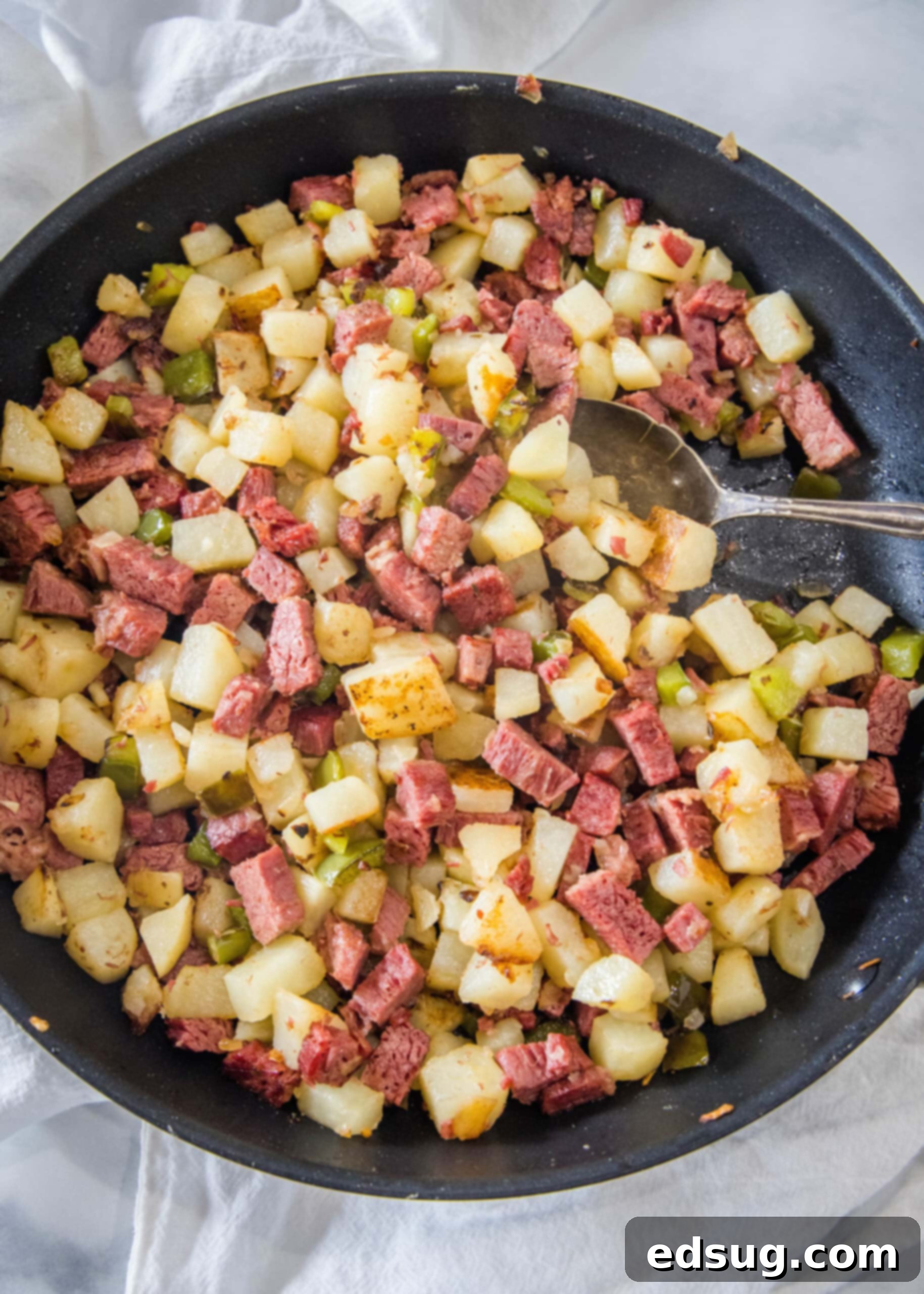 Make homemade corned beef hash with leftover corned beef, tender potatoes, onions, and bell peppers. An easy breakfast, ready in 30 minutes! Overhead view of perfectly cooked corned beef hash in a large skillet with a serving spoon, golden brown and inviting.