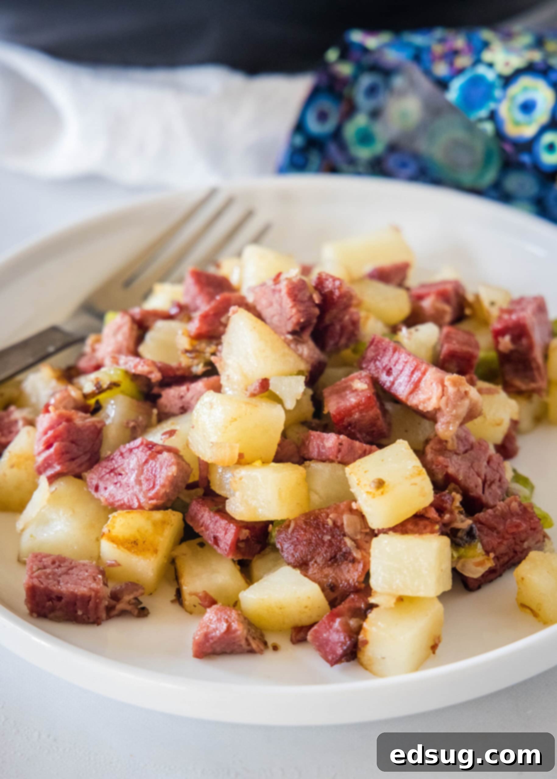 Make homemade corned beef hash with leftover corned beef, tender potatoes, onions, and bell peppers. An easy breakfast, ready in 30 minutes! A perfectly portioned serving of corned beef hash on a white plate next to a fork, ready to be enjoyed.