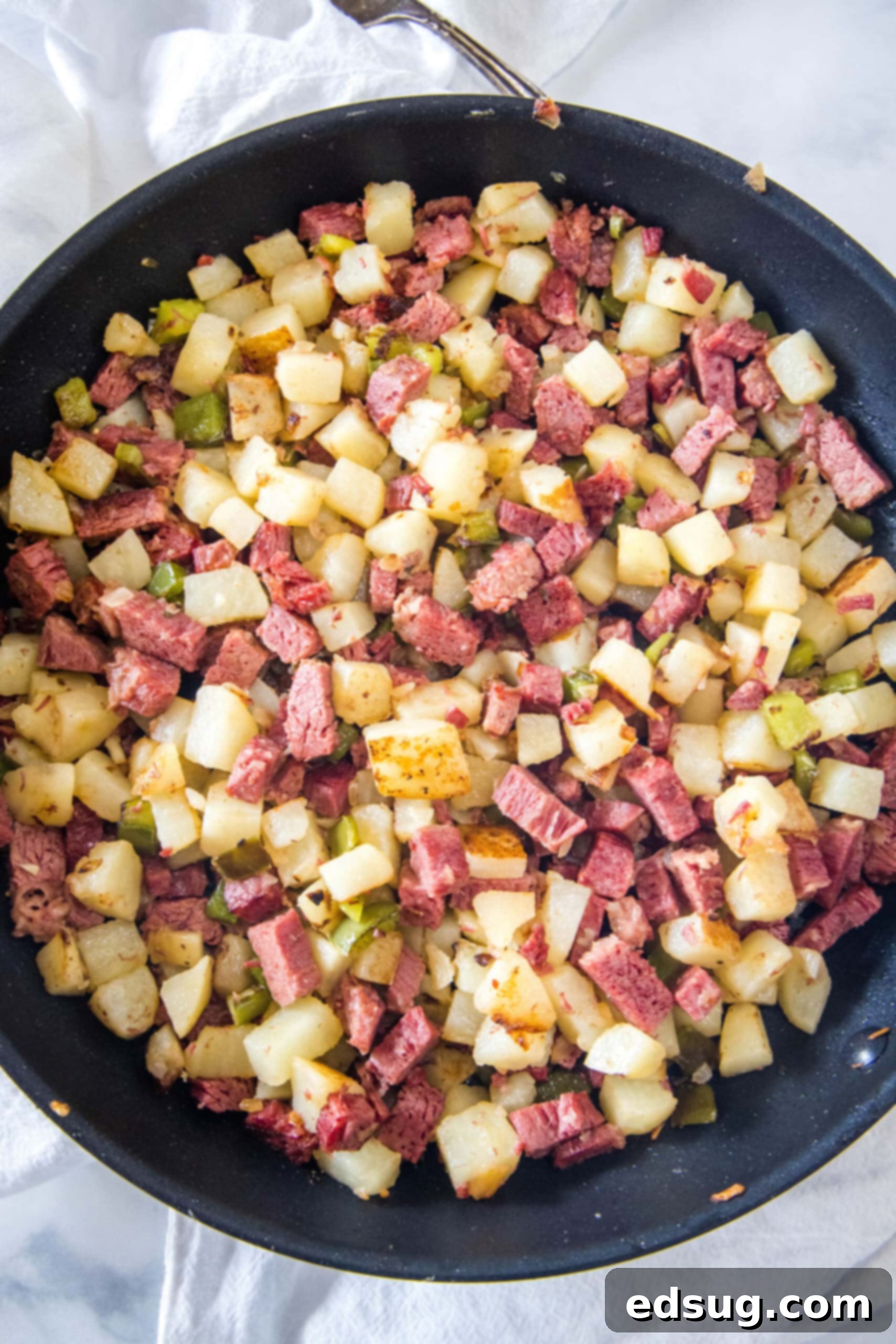 Make homemade corned beef hash with leftover corned beef, tender potatoes, onions, and bell peppers. An easy breakfast, ready in 30 minutes! Overhead view of diced potatoes, chopped corned beef, onions, and bell peppers combined in a skillet, ready to be cooked into hash.