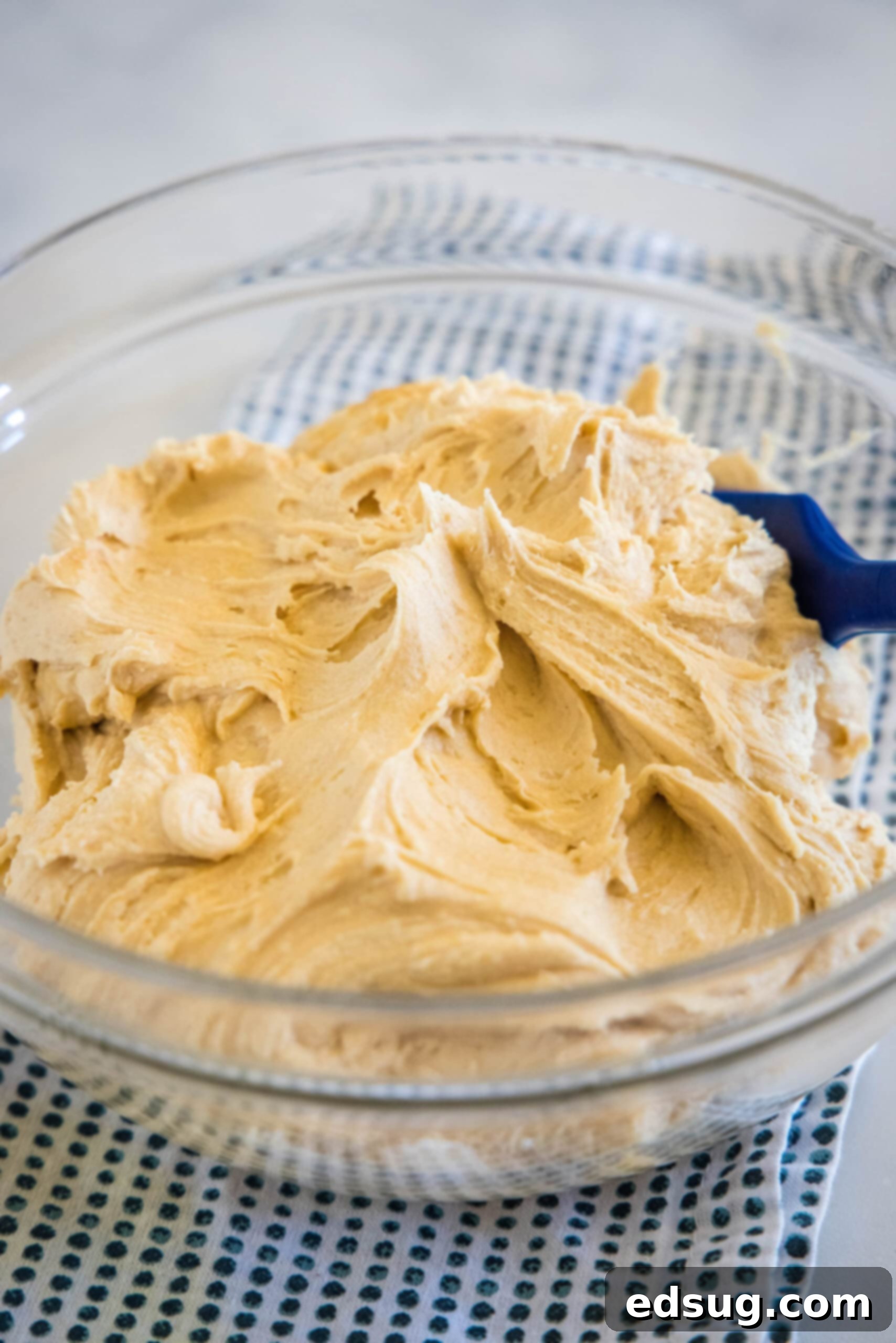 Homemade peanut butter frosting is smooth, creamy, and perfect for decorating cakes and cupcakes. Ready in minutes with just 5 ingredients! Peanut butter frosting in a glass bowl with a blue stirring spoon.