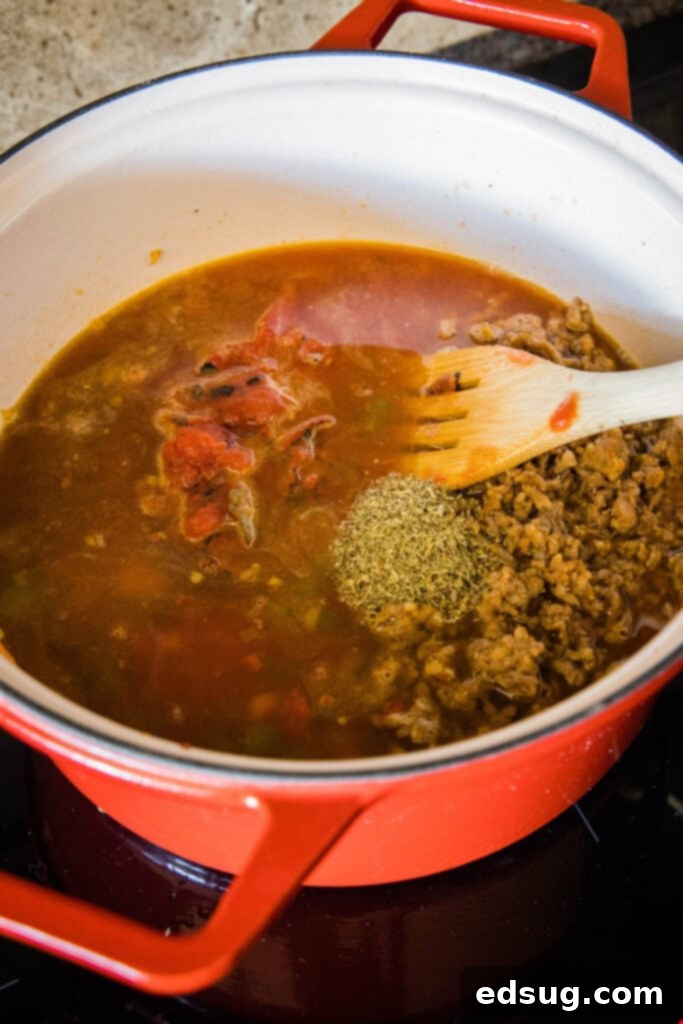 Italian sausage soup simmering gently in a large pot, with a wooden spoon stirring it.