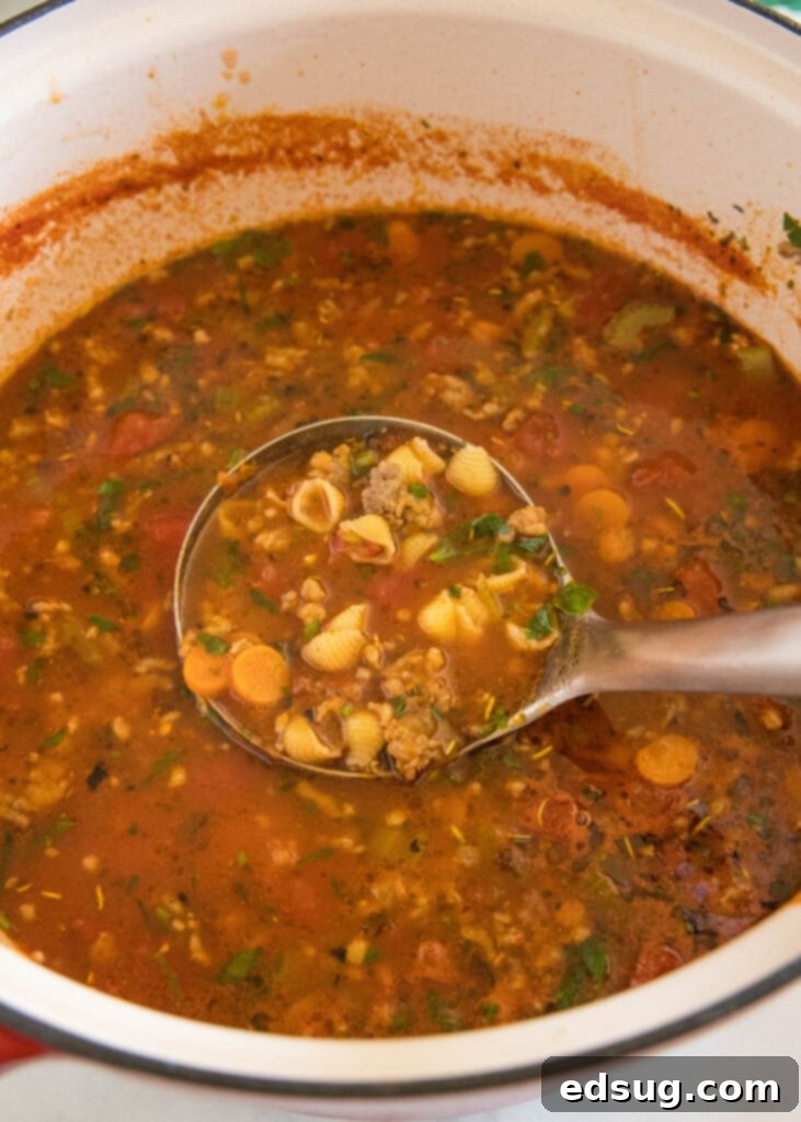 A ladle scooping a generous portion of Italian sausage soup from a large pot, ready to serve.