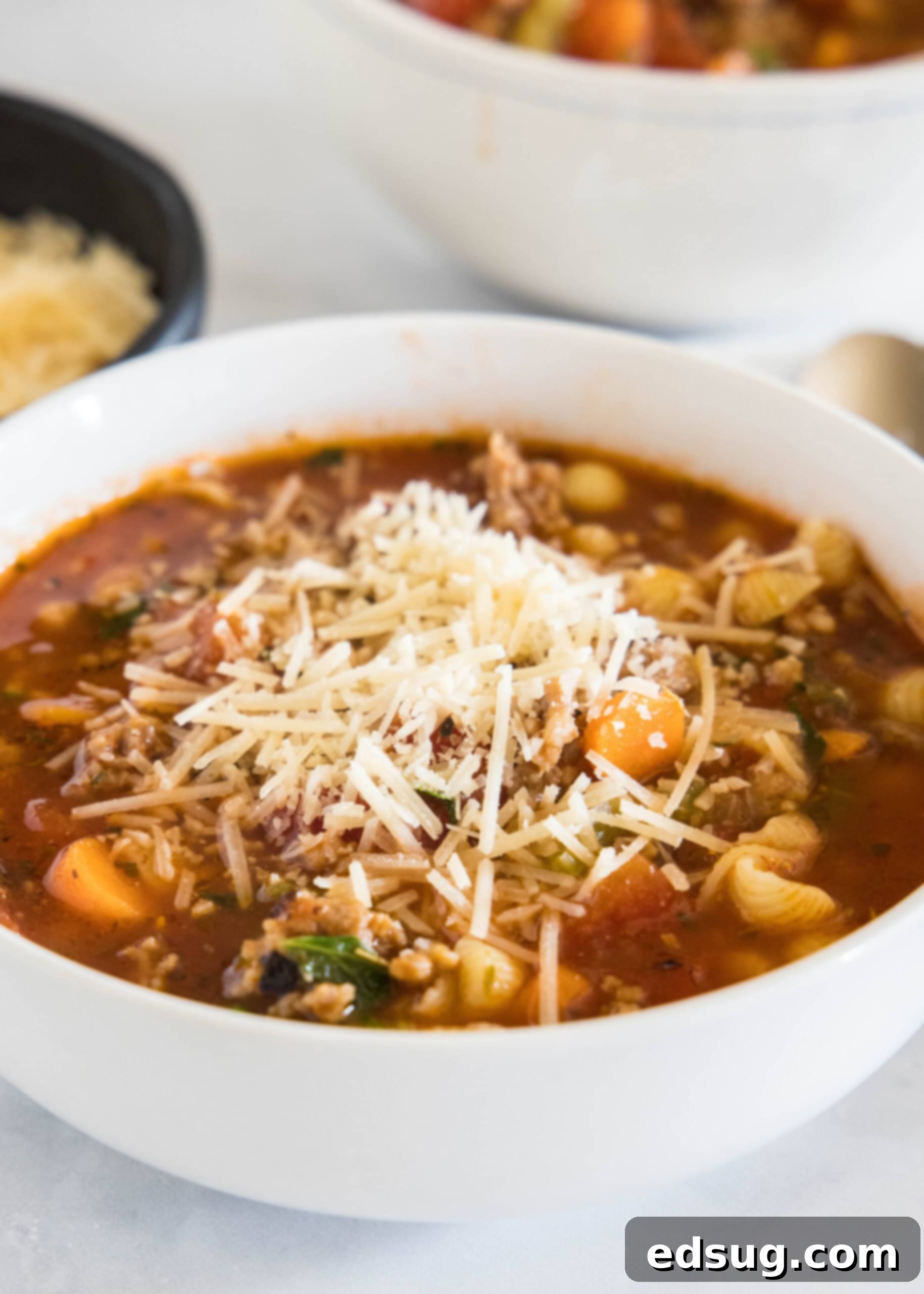 A beautifully plated bowl of Italian sausage soup, garnished with shredded Parmesan cheese and fresh herbs.