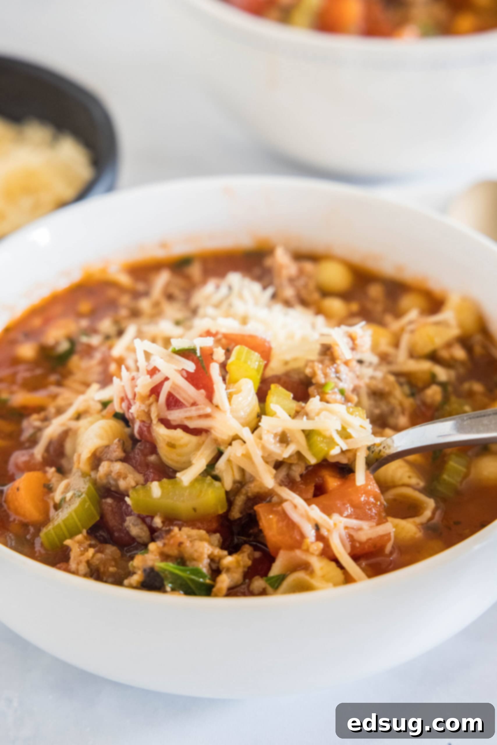 A close-up shot of Italian sausage soup in a bowl, with a spoon, highlighting the steam rising and the texture of the ingredients.