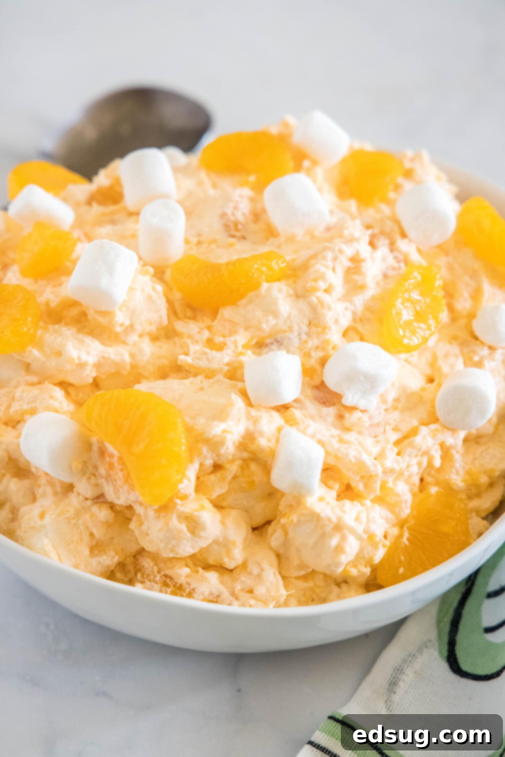 Orange fluff salad topped with mini marshmallows in a white bowl.