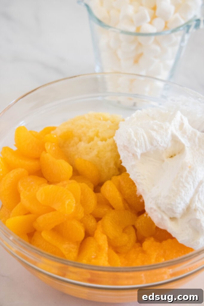 Canned mandarin oranges, crushed pineapple, and Cool Whip added to a glass bowl.