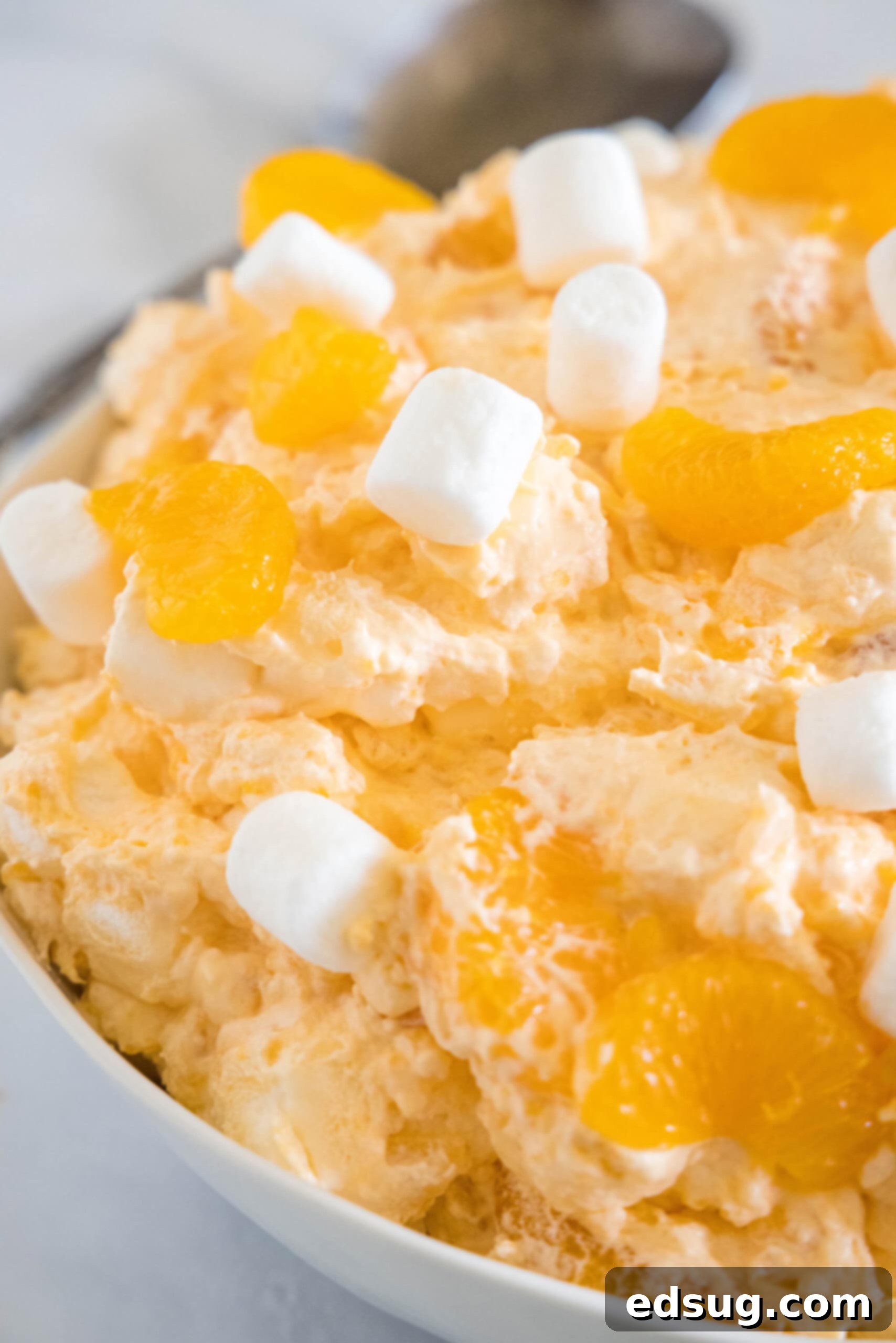 Close up of orange fluff salad topped with mini marshmallows in a white bowl.