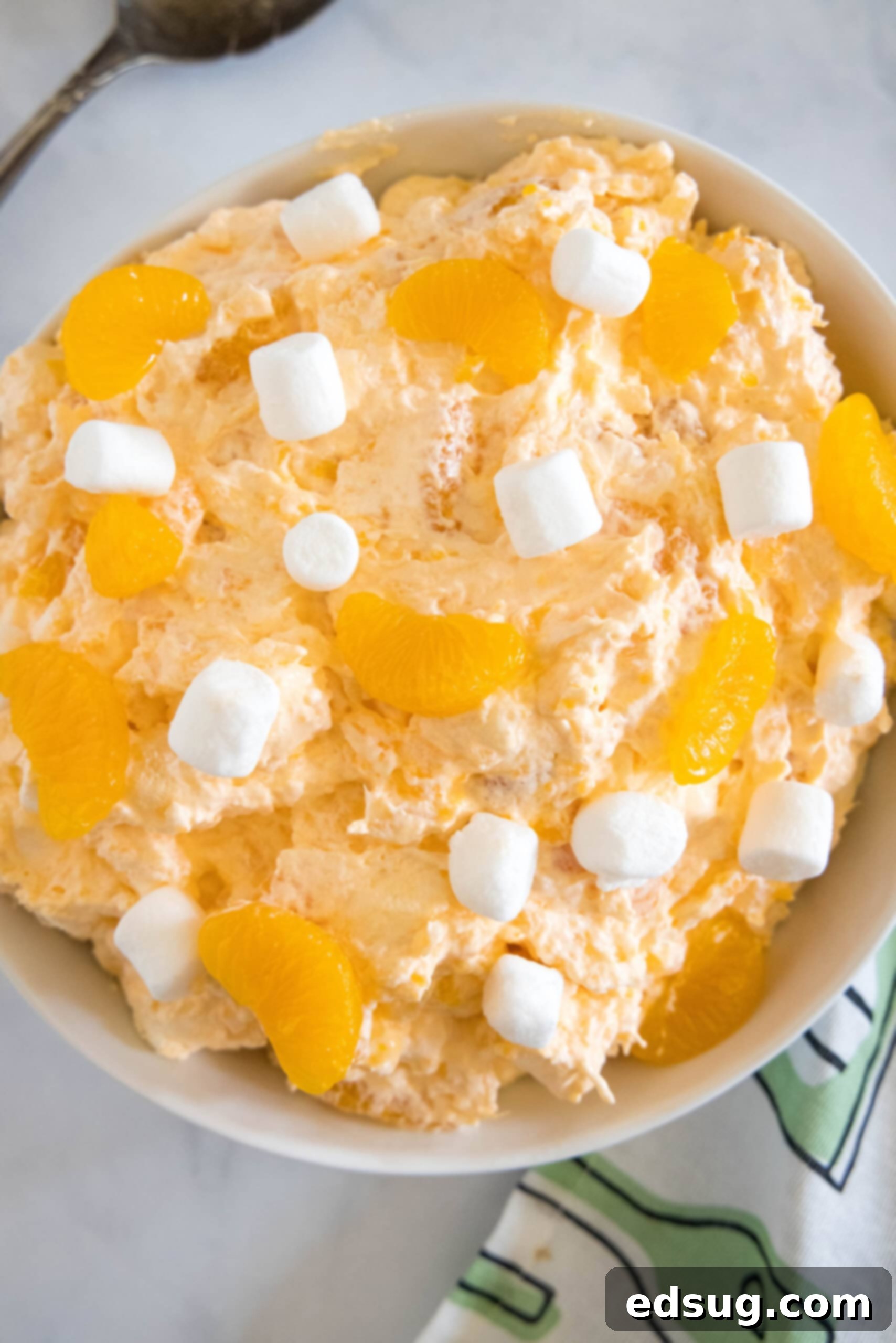Overhead view of orange fluff salad topped with mini marshmallows in a white bowl.