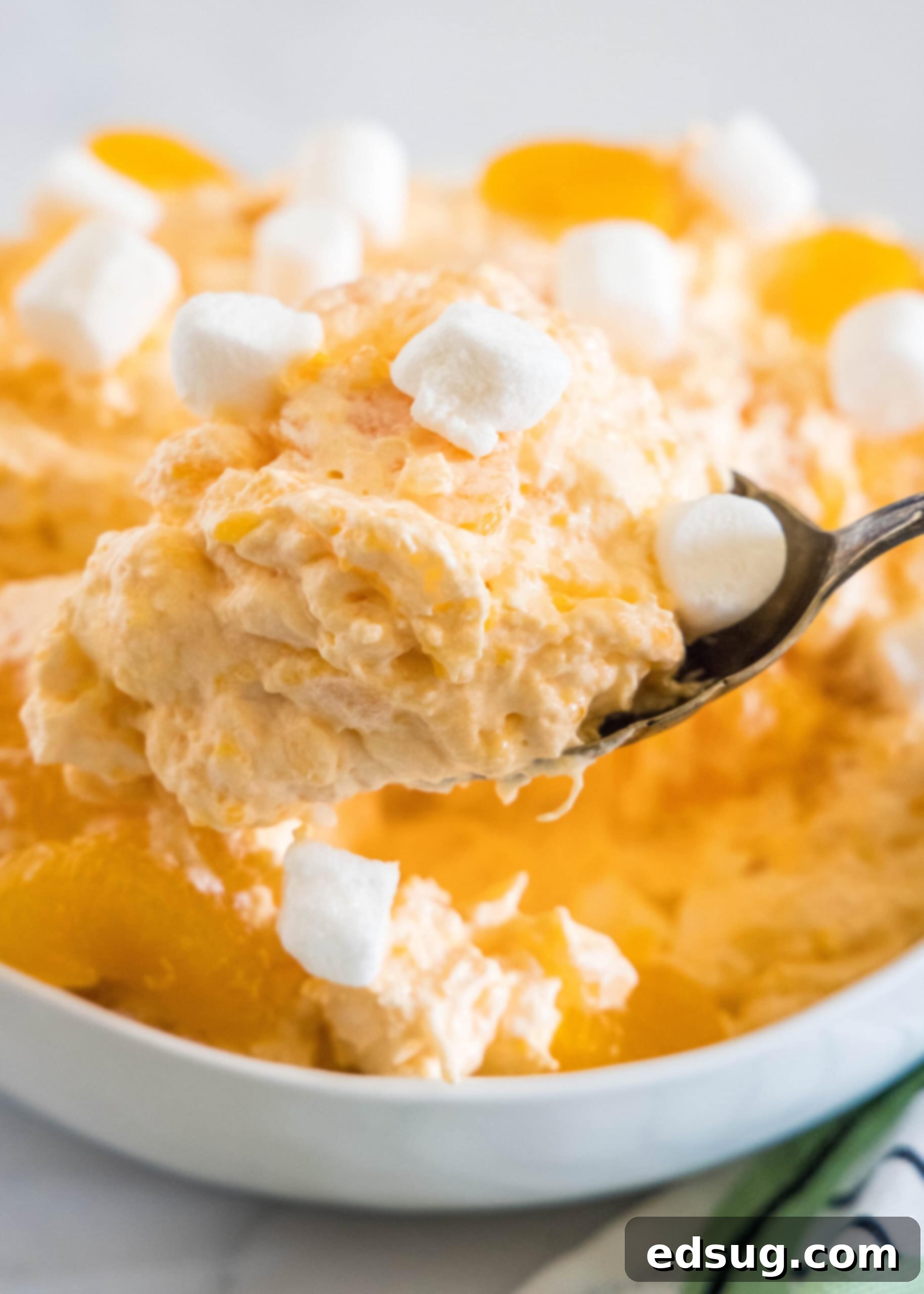 A spoon scooping orange fluff salad from a bowl.