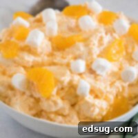 Orange fluff salad topped with mini marshmallows in a white bowl.