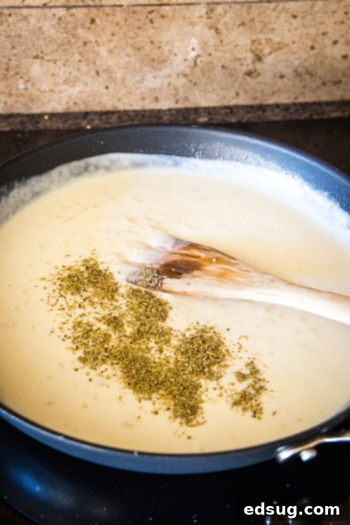 Make this casserole-style cheesy chicken spaghetti with Rotel tomatoes, juicy chicken, and tender pasta baked in a flavorful creamy sauce. Seasoning added to cream sauce in a skillet, with a wooden spoon.