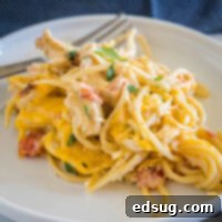 A serving of chicken spaghetti on a white plate with a fork in the background.