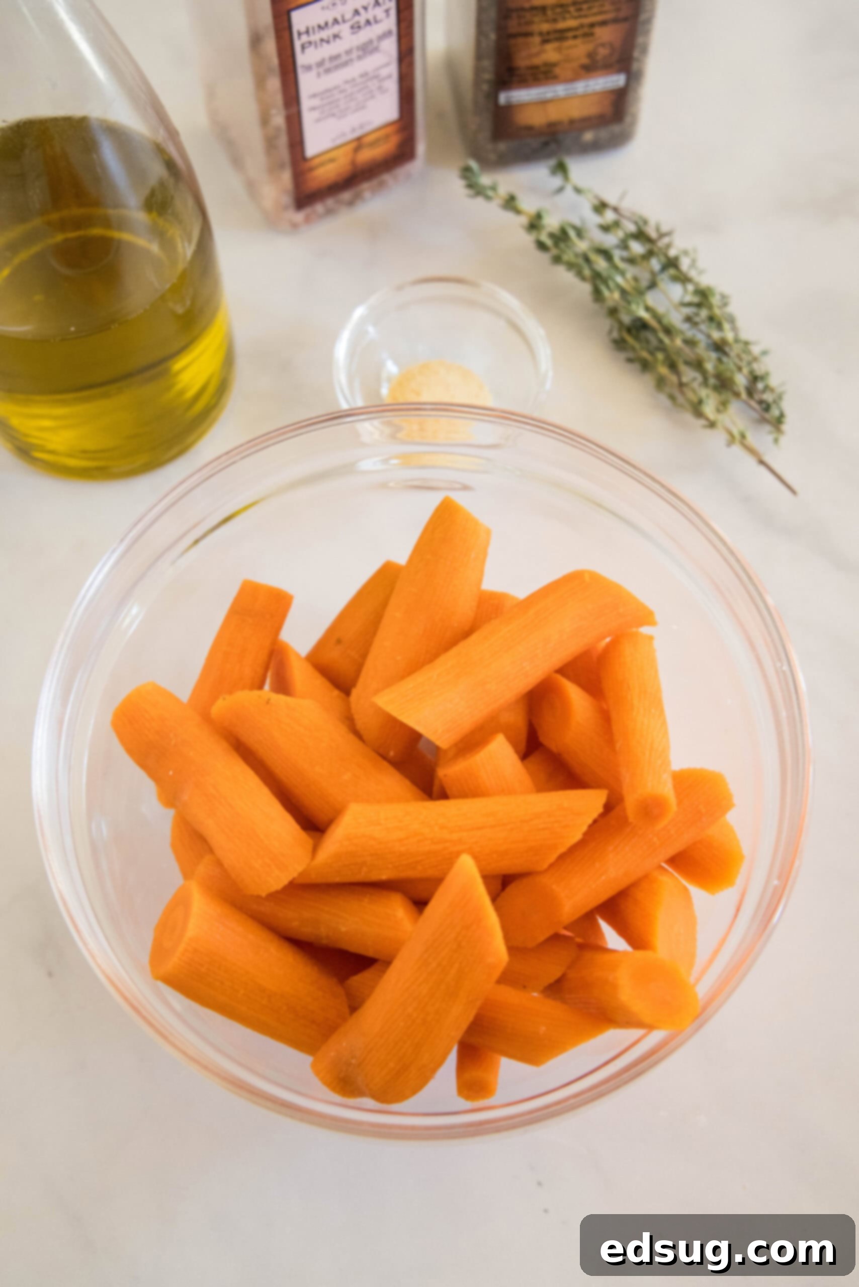 These tender oven roasted carrots come out crispy, caramelized, and full of flavor. They're the perfect easy side dish for any occasion! Ingredients for making oven roasted carrots, including fresh carrots, olive oil, garlic powder, salt, pepper, and fresh thyme.