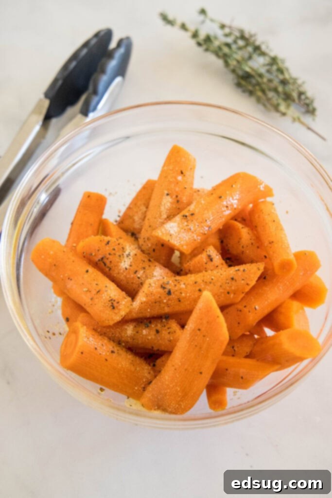 These tender oven roasted carrots come out crispy, caramelized, and full of flavor. They're the perfect easy side dish for any occasion! Raw carrots tossed in olive oil and seasoning in a glass bowl, prepped for roasting.