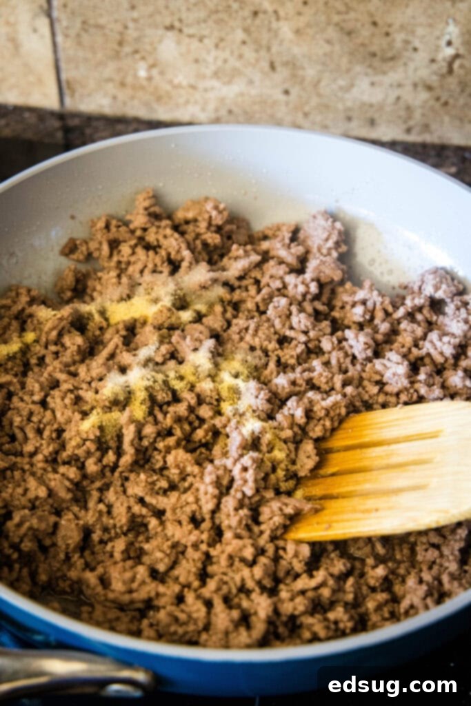 Tuck into a crispy cheeseburger quesadilla loaded with juicy burger meat, onions, pickles, and melty cheese folded inside a warm tortilla. A wooden spatula stirring ground beef as it cooks in a skillet.