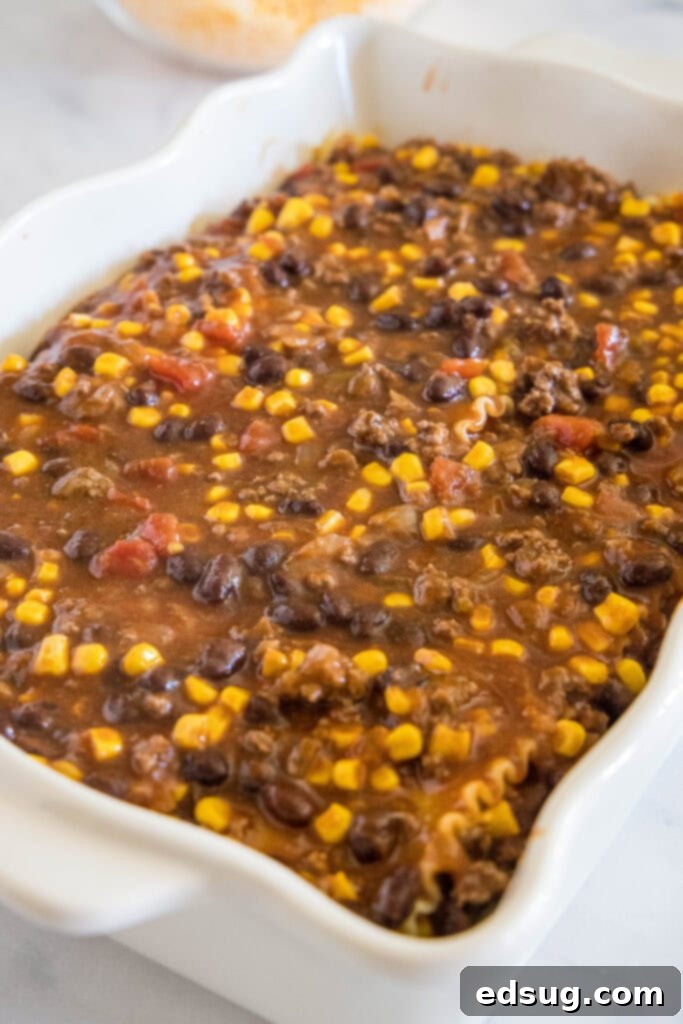 This Mexican lasagna has layers of Tex-Mex flavor, with savory beef, corn, beans, enchilada sauce, and cheese baked between lasagna noodles. Multiple layers of Mexican lasagna, featuring noodles, beef filling, and cheese, neatly stacked in a white ceramic baking dish before baking.