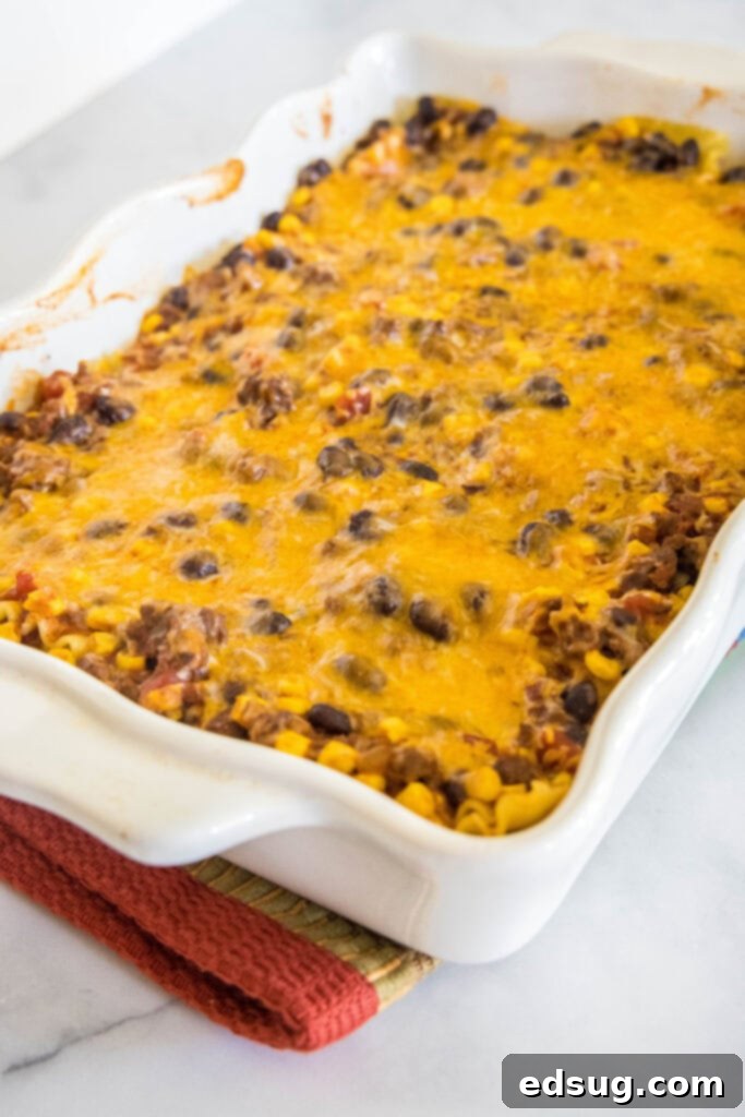 This Mexican lasagna has layers of Tex-Mex flavor, with savory beef, corn, beans, enchilada sauce, and cheese baked between lasagna noodles. Freshly baked Mexican lasagna, hot and bubbling, in a white ceramic baking dish, ready to be served.