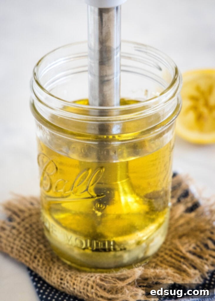 An immersion blender actively blending the ingredients for homemade mayonnaise inside a glass mason jar, creating a thick, creamy texture.