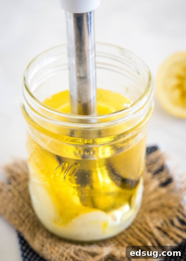 Close-up shot of an immersion blender continuing to blend homemade mayo ingredients, showing the creamy transformation within the glass jar.