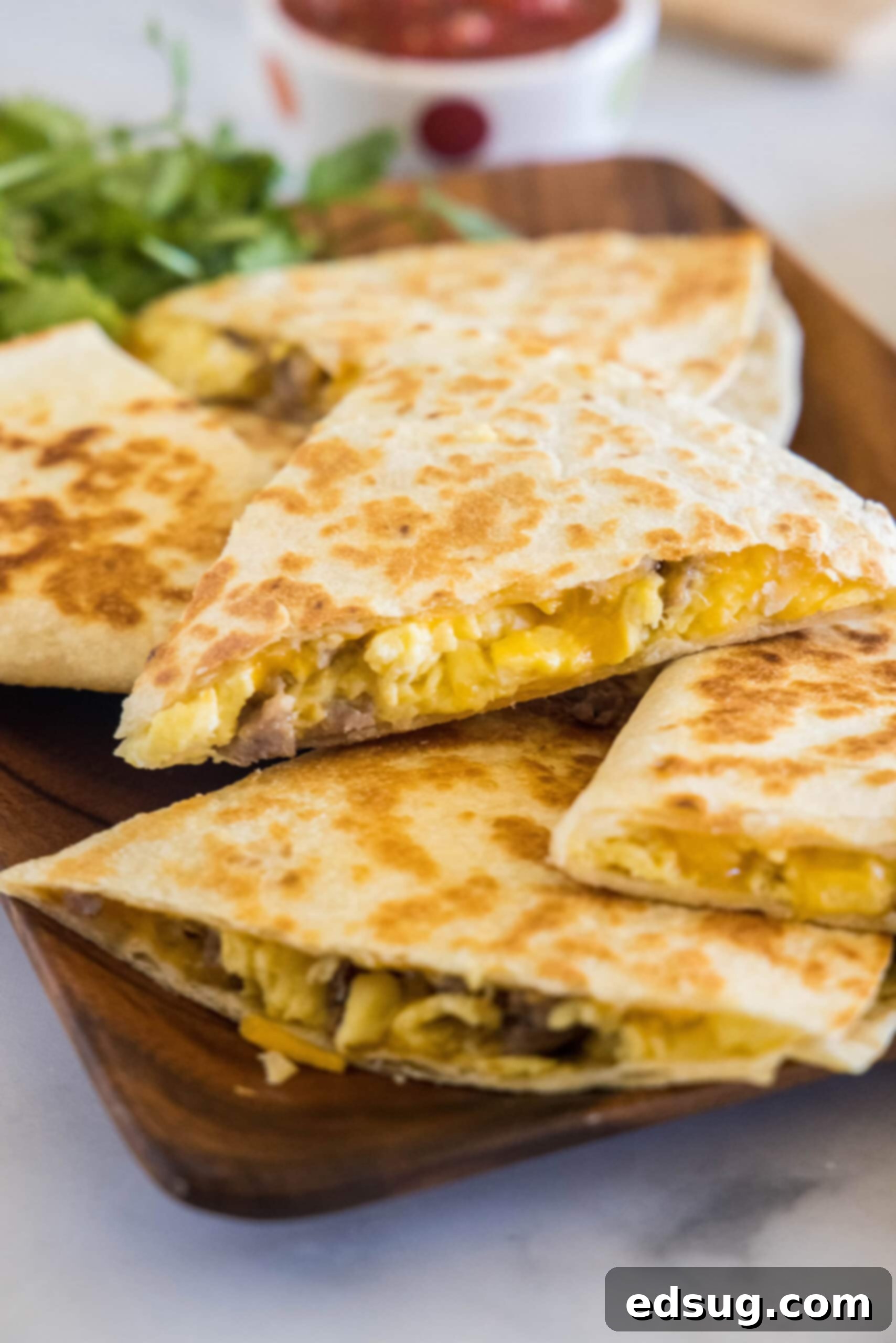 Rise and shine with this easy breakfast quesadilla recipe! Made with eggs, savory sausage, and melty cheese folded between warm tortillas. Stacked breakfast quesadillas on a wooden serving platter, ready to be enjoyed.
