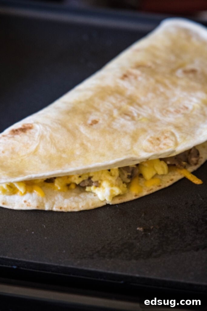 Rise and shine with this easy breakfast quesadilla recipe! Made with eggs, savory sausage, and melty cheese folded between warm tortillas. A folded breakfast quesadilla cooking on a griddle, browning beautifully.