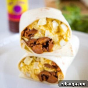 Two halves of a chorizo breakfast burrito stacked on a plate, showing the eggs, cheese, potatoes, and chorizo filling inside.