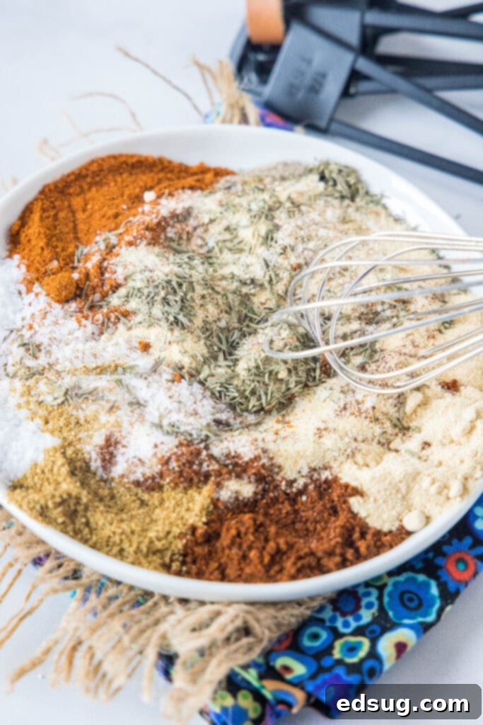 A close-up of various spices being mixed together on a clean plate, illustrating the homemade chicken seasoning preparation.