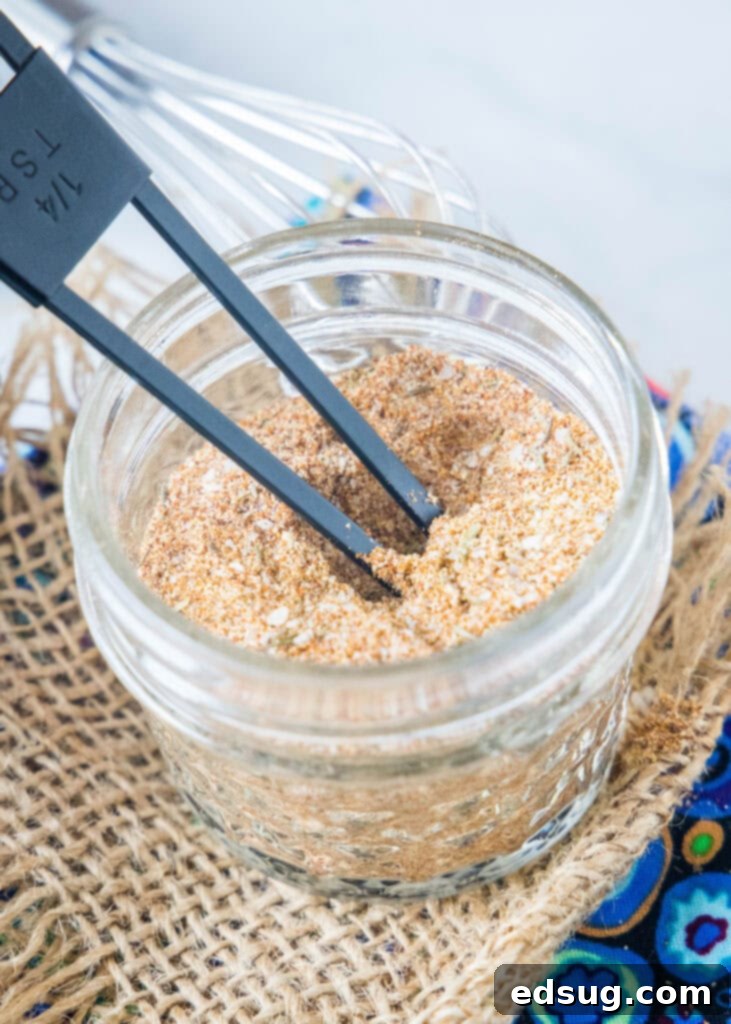 A spoon in a clear glass jar of the homemade chicken seasoning, showcasing its rich color and texture.
