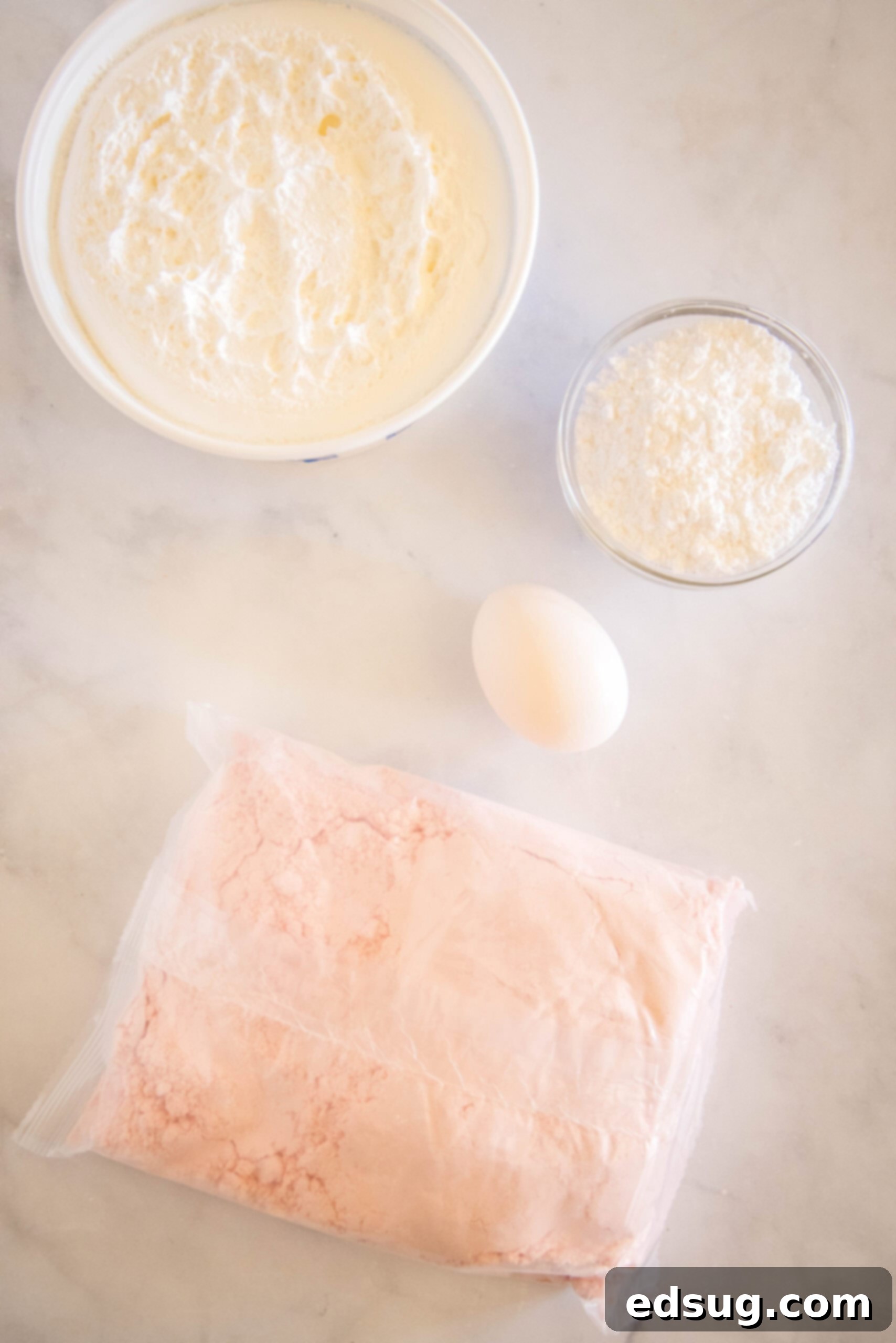 Ingredients for Cool Whip cookies laid out on a kitchen counter: a box of cake mix, a tub of Cool Whip, a single egg, and a bowl of powdered sugar. All you need for these simple cake mix cookies.