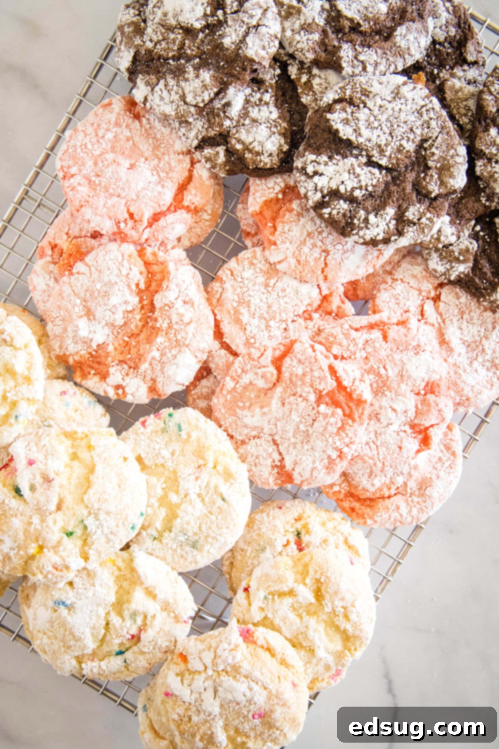 Overhead view of an assortment of freshly baked Cool Whip cookies cooling on a wire rack, displaying different flavors and perfect crinkles.