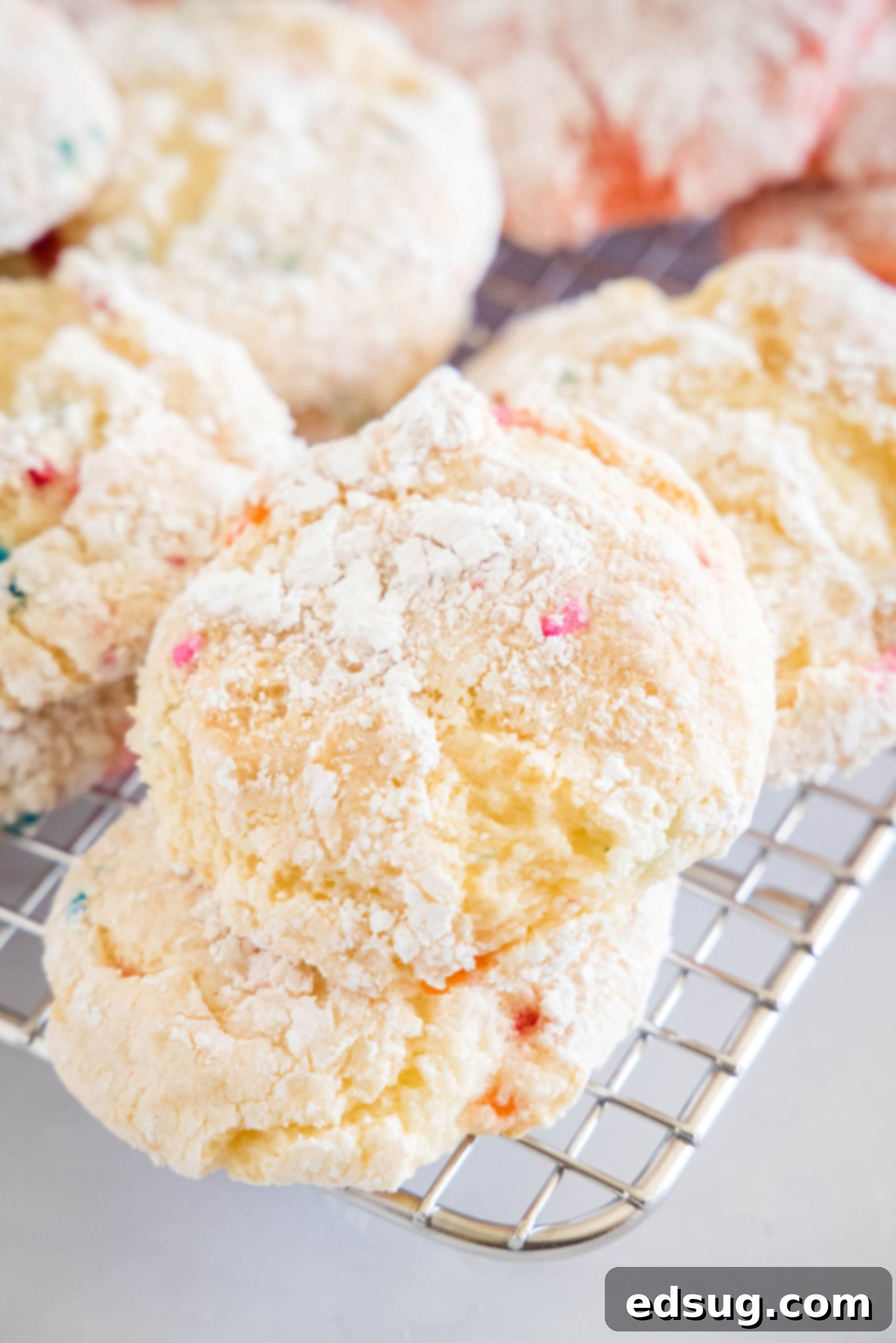Close up shot of vibrant funfetti Cool Whip cookies on a wire rack, showing colorful sprinkles and delicate crinkles from powdered sugar.