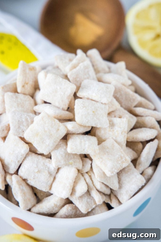 A bowl filled with bright yellow lemon muddy buddies, dusted with powdered sugar and lemon zest, ready to be enjoyed.