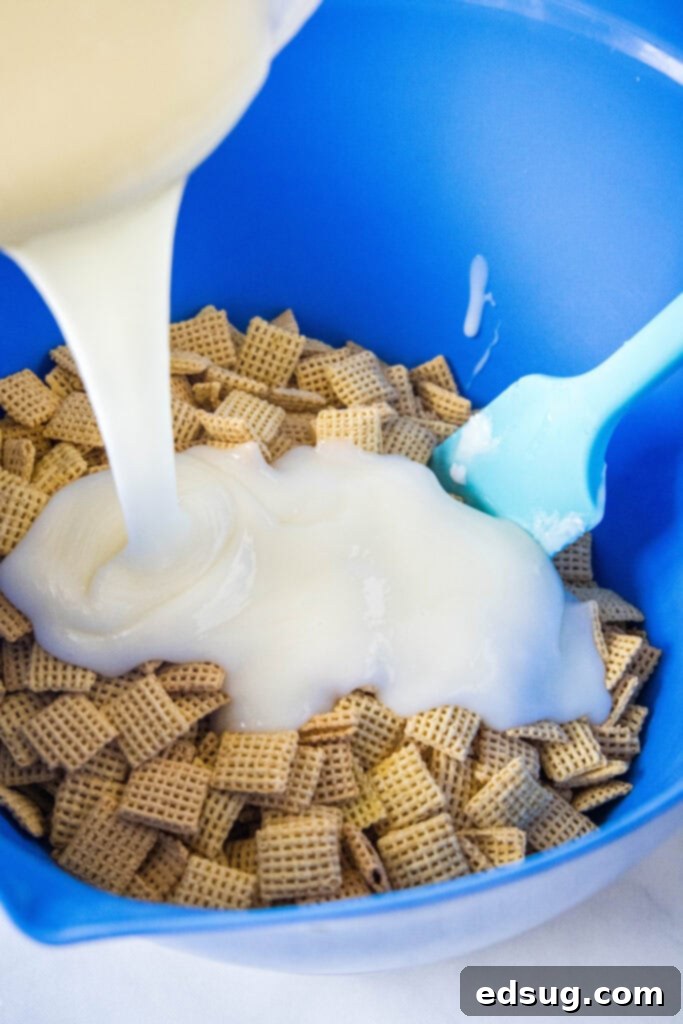 A close-up shot of white chocolate mixture being poured over a large bowl of Chex cereal, ready to be mixed for the lemon puppy chow.