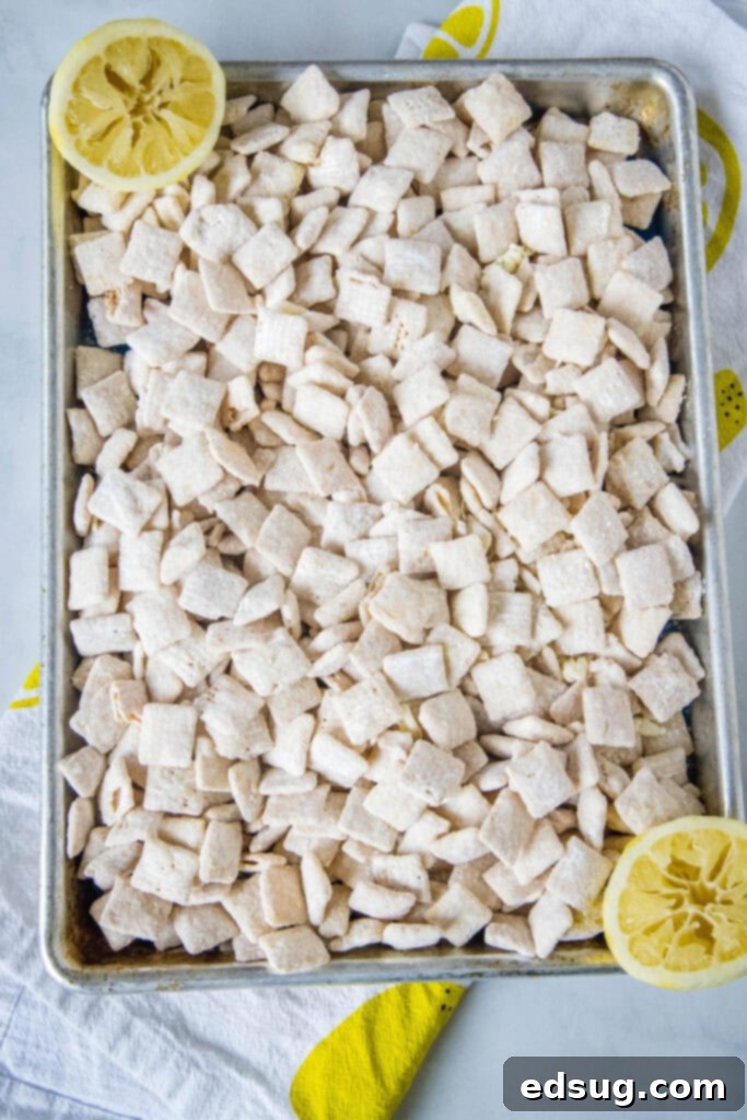 An overhead shot of a baking sheet filled with a generous amount of finished lemon puppy chow, showing its vibrant yellow color and powdered sugar coating.